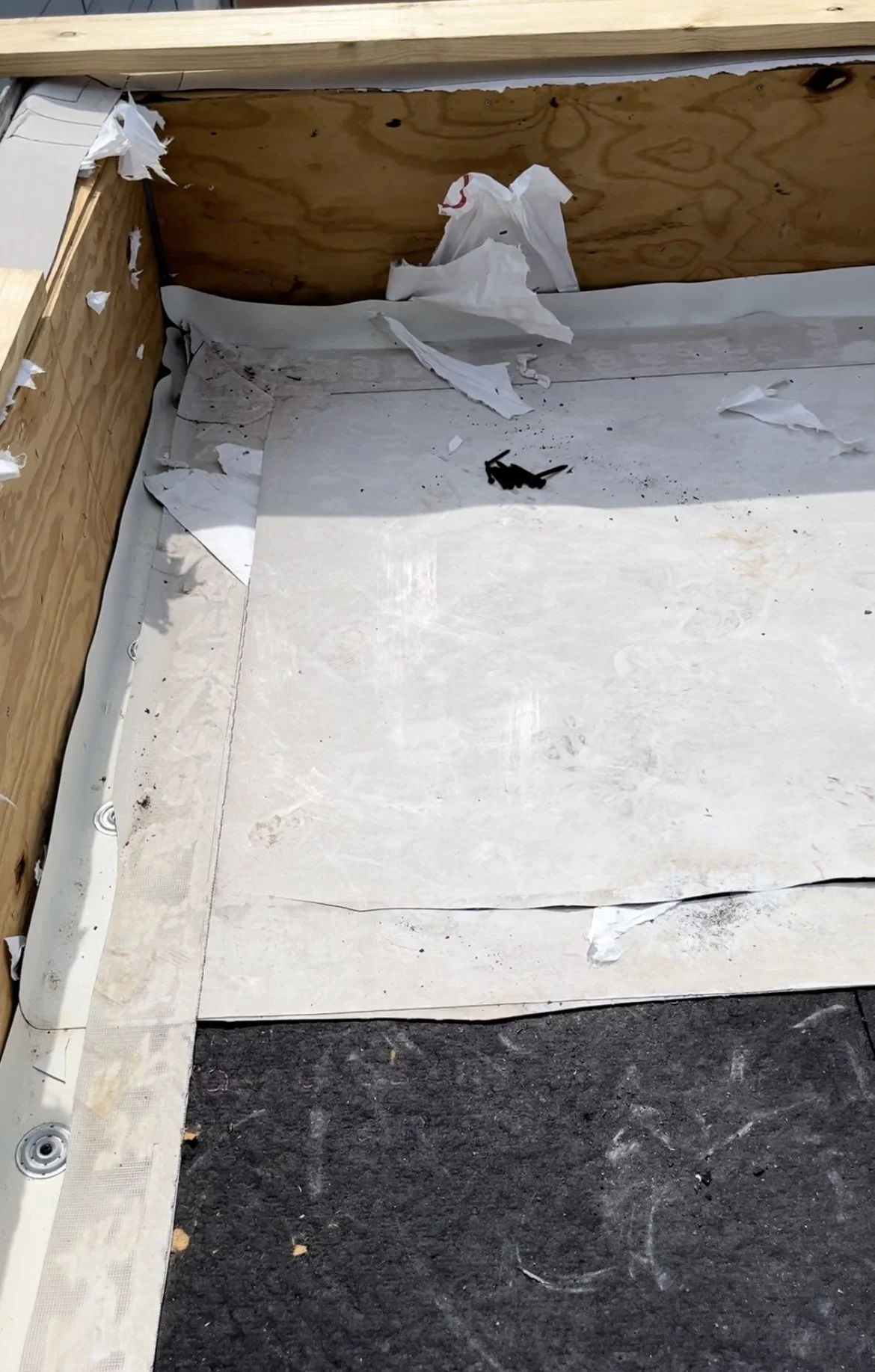 Roof construction site with plywood walls, insulation material, debris, and screws.