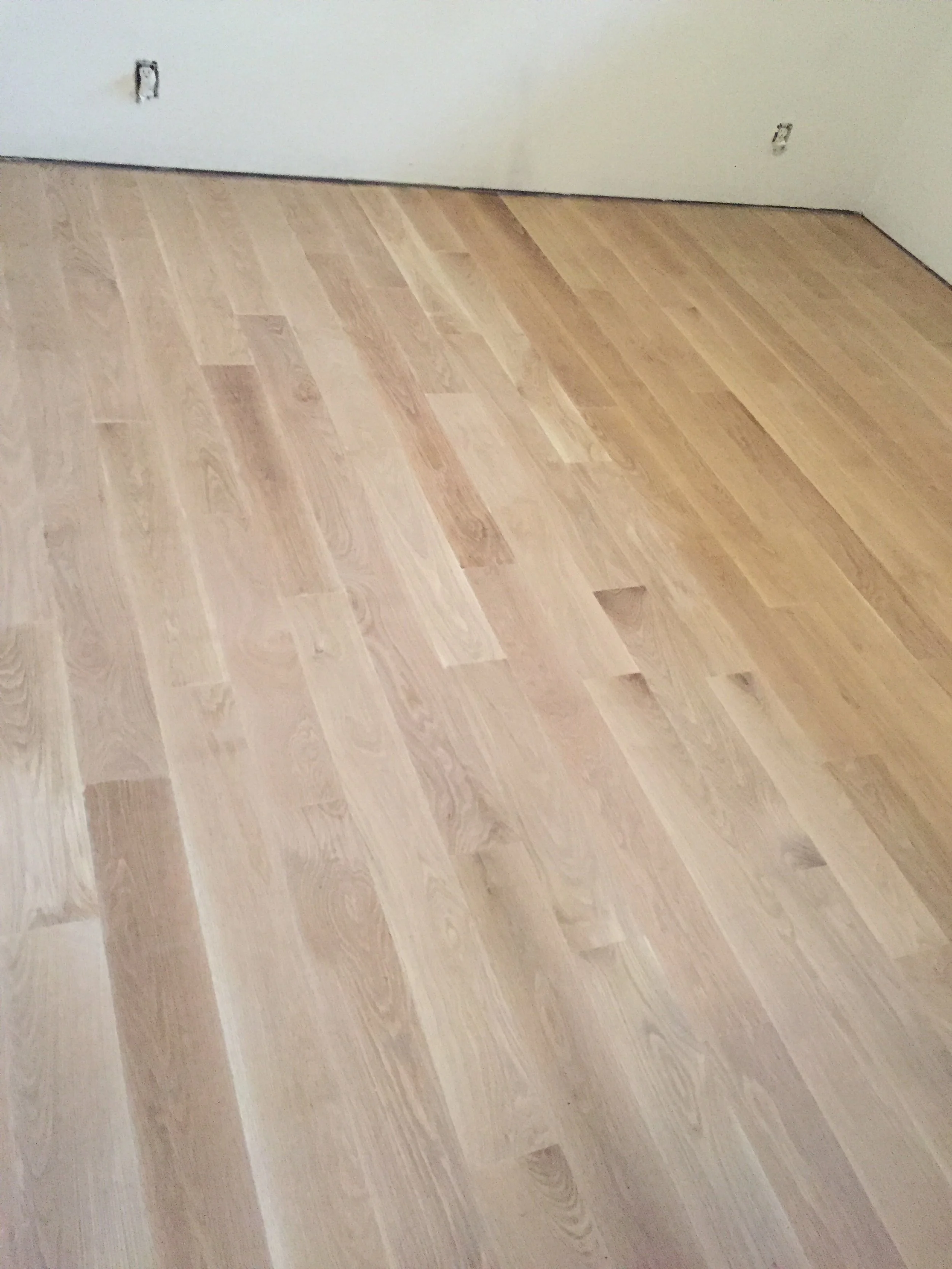 Newly installed light wood flooring in an empty room with white walls.