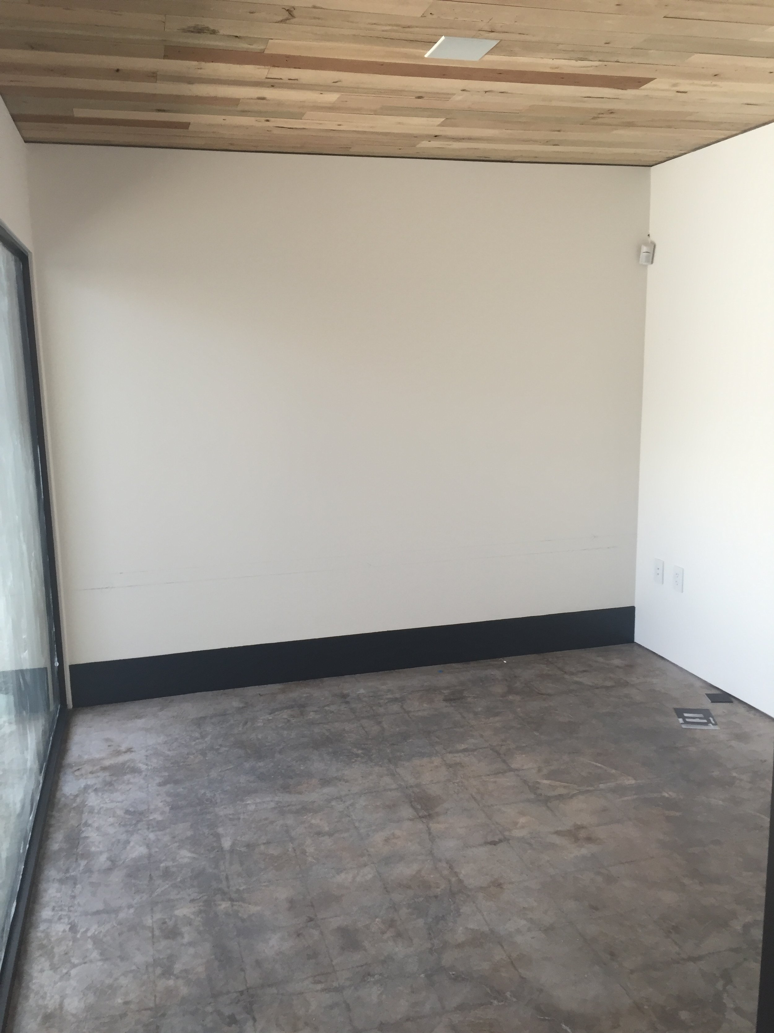 Empty room with concrete floor, white walls, and wooden ceiling