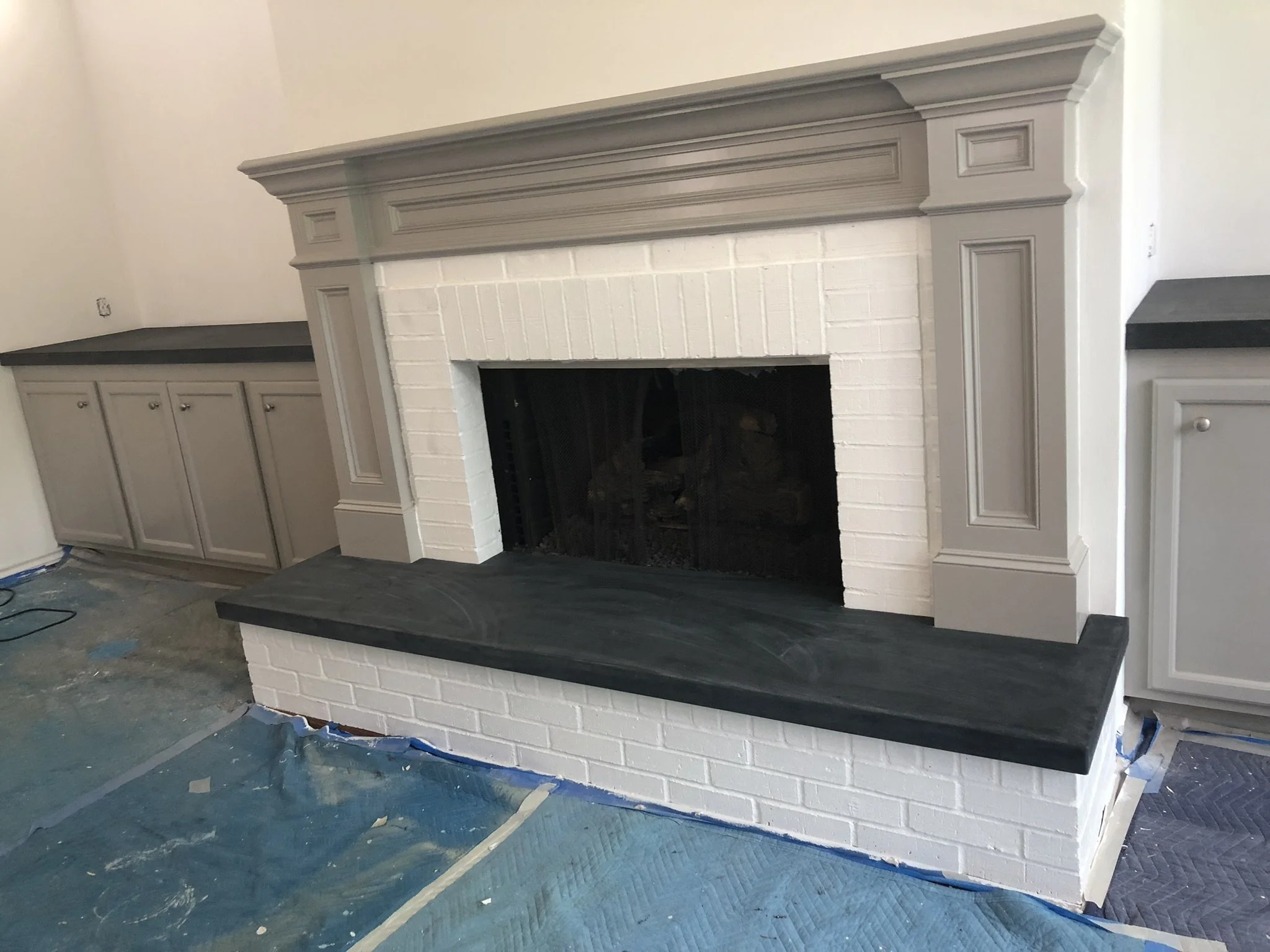 Renovated fireplace with gray mantel and white brick surround, flanked by built-in cabinetry with gray countertops in a room under construction.