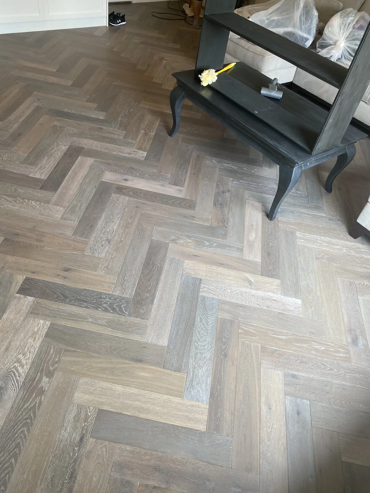 Herringbone wooden flooring with a black table and dusting brush on top.