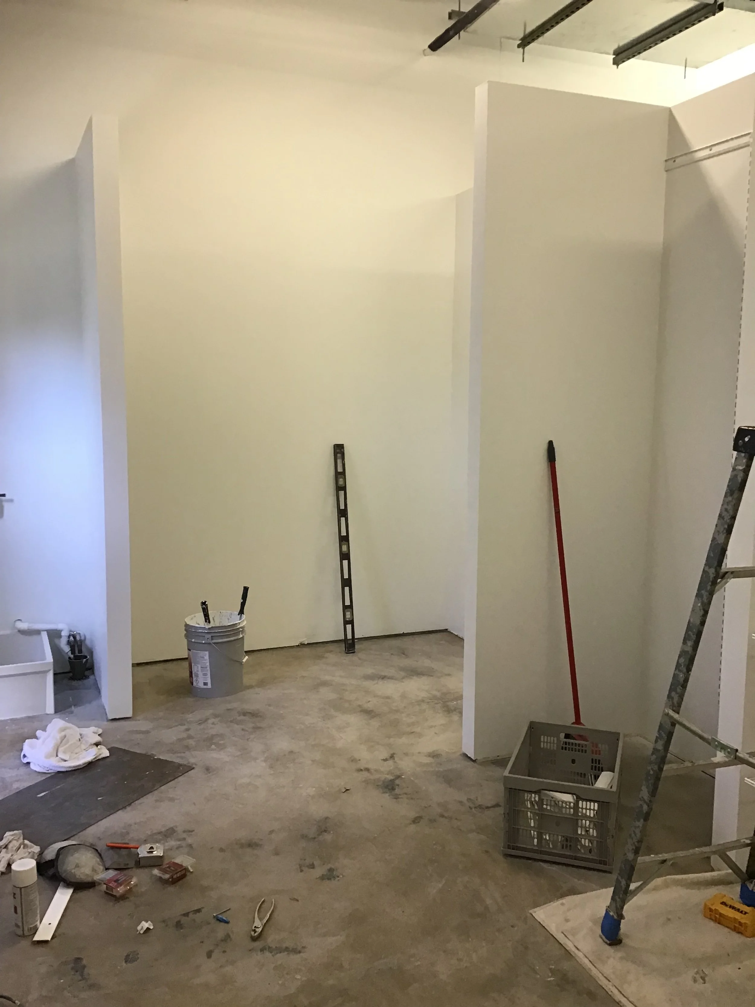 Construction site with unfinished walls, a paint bucket, level tool, ladder, and various tools on the floor.