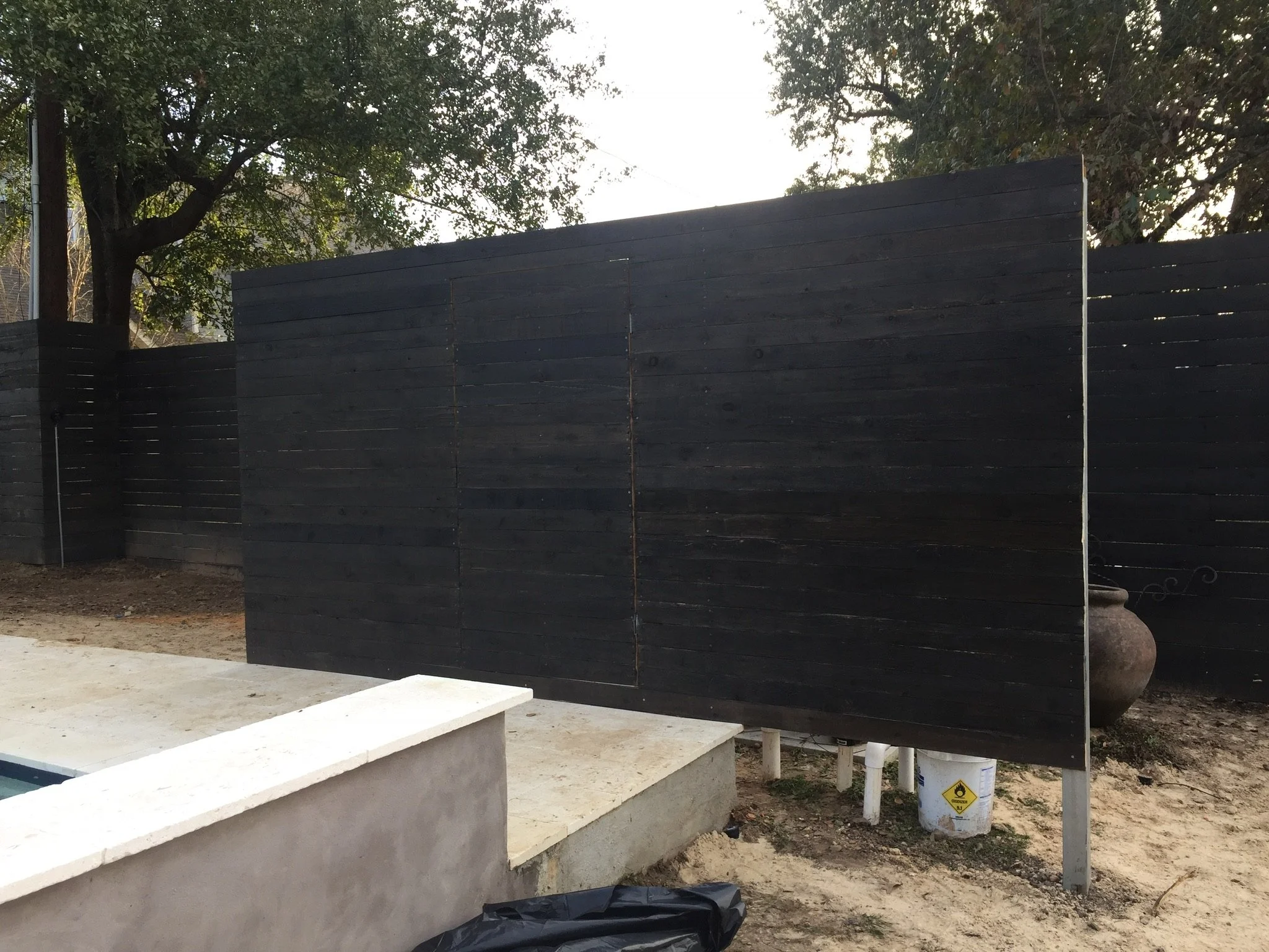 Dark wooden privacy fence near concrete pool border with trees in the background.