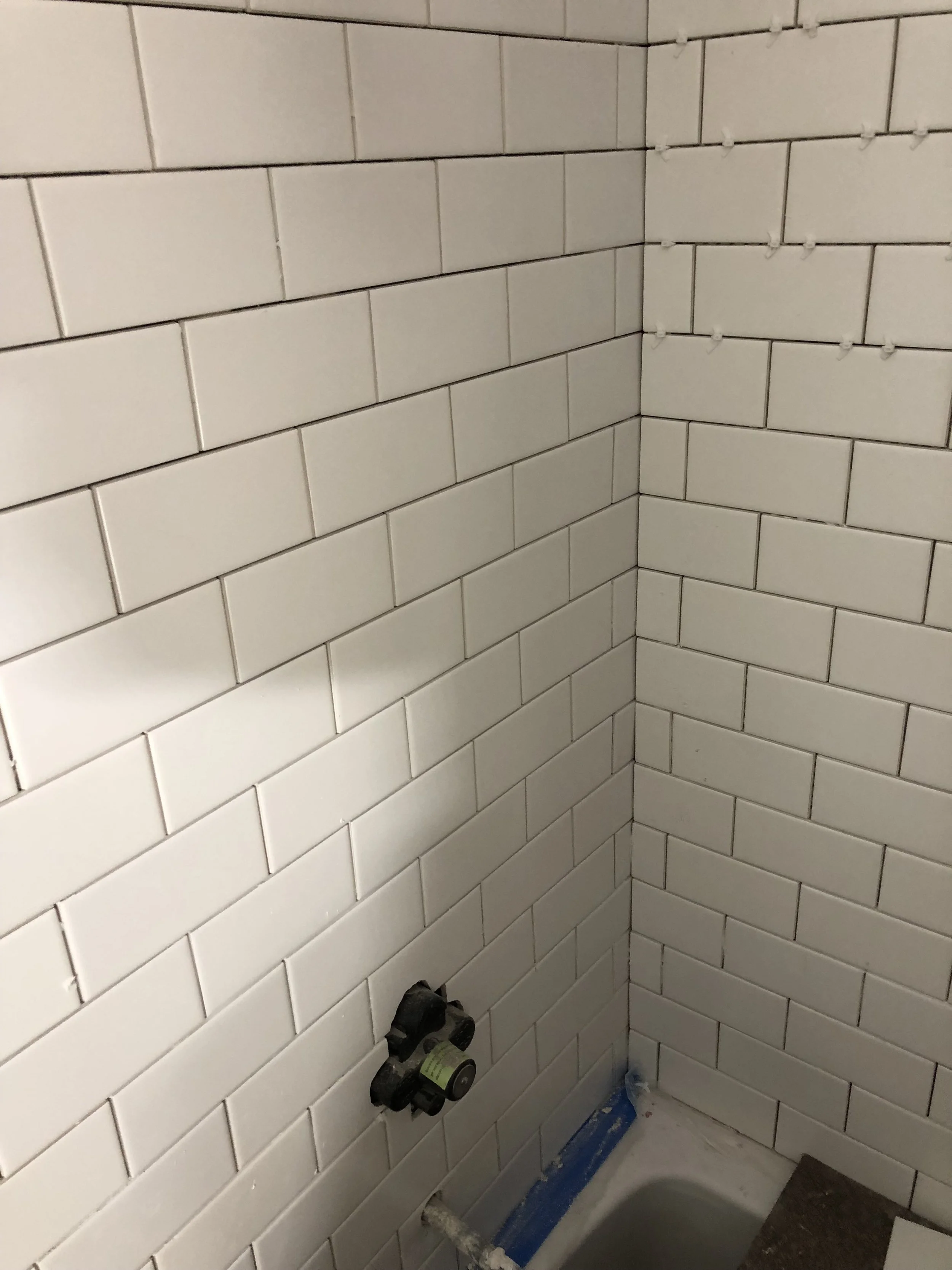 White subway tile wall with partially installed plumbing fixtures in a bathroom.