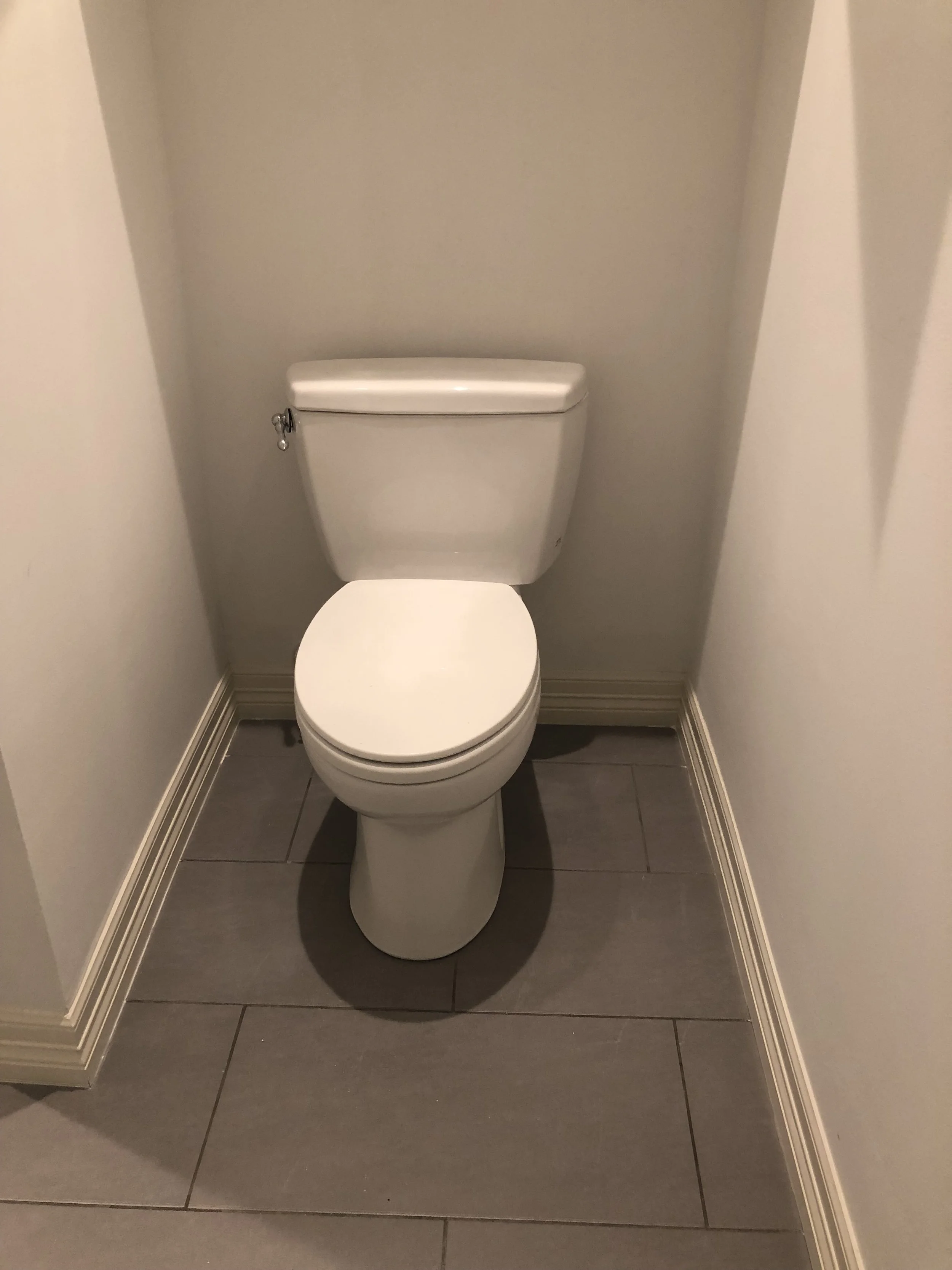 A white toilet in a narrow bathroom with gray tile floor and white walls.