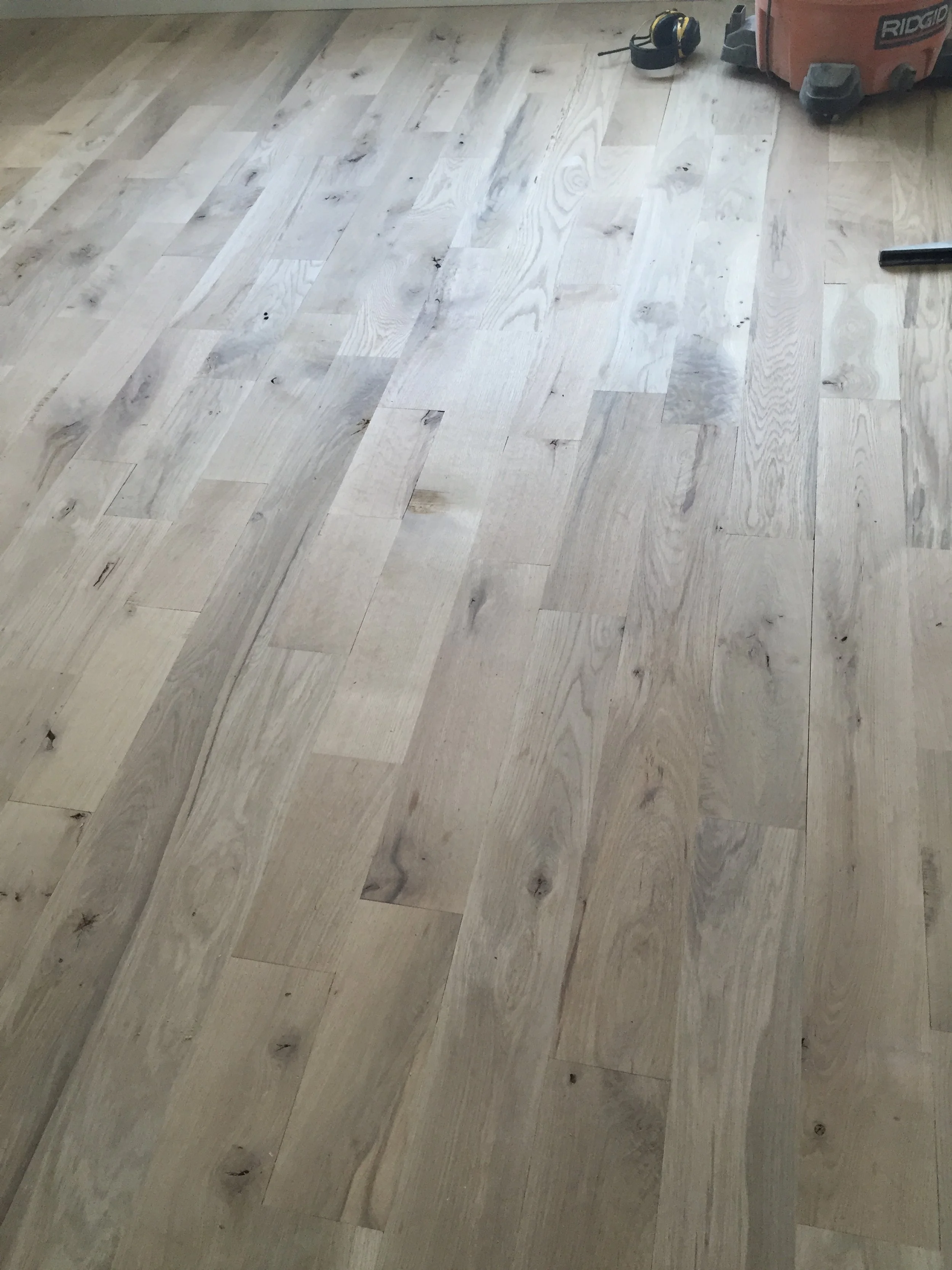 Hardwood floor installation with a vacuum cleaner in the background.