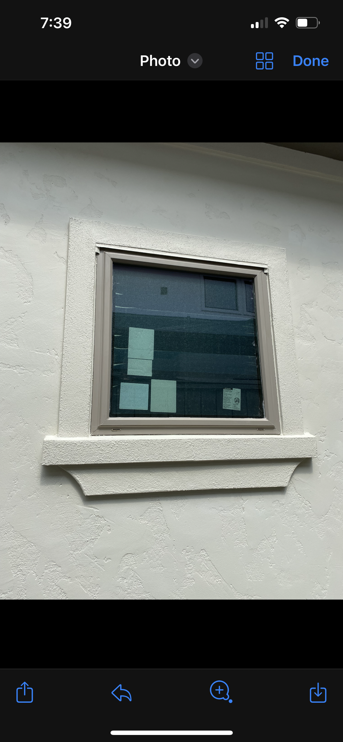 A small window on a stucco wall with a beige frame and decorative trim underneath.