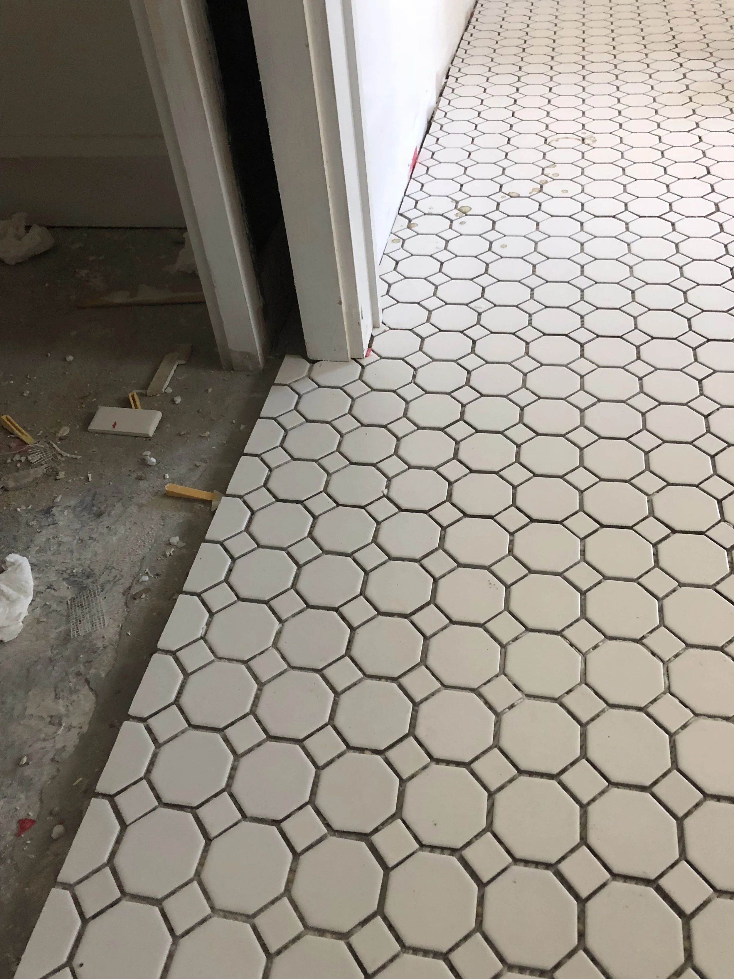 White hexagonal floor tiles in a hallway under construction with debris on the side.