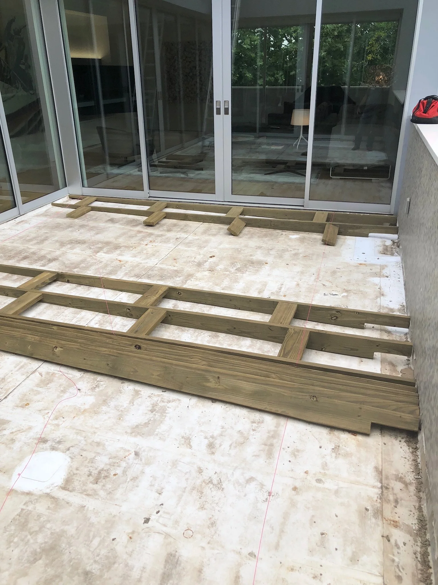 Construction site with wooden deck frames on a concrete floor in front of sliding glass doors.