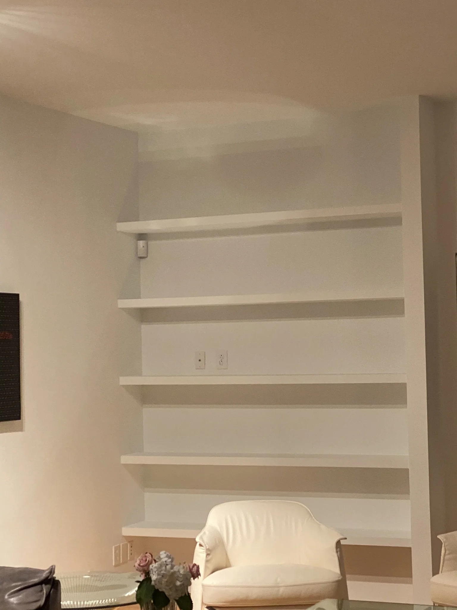 Minimalist room with white shelves, a white armchair, and a glass table with flowers