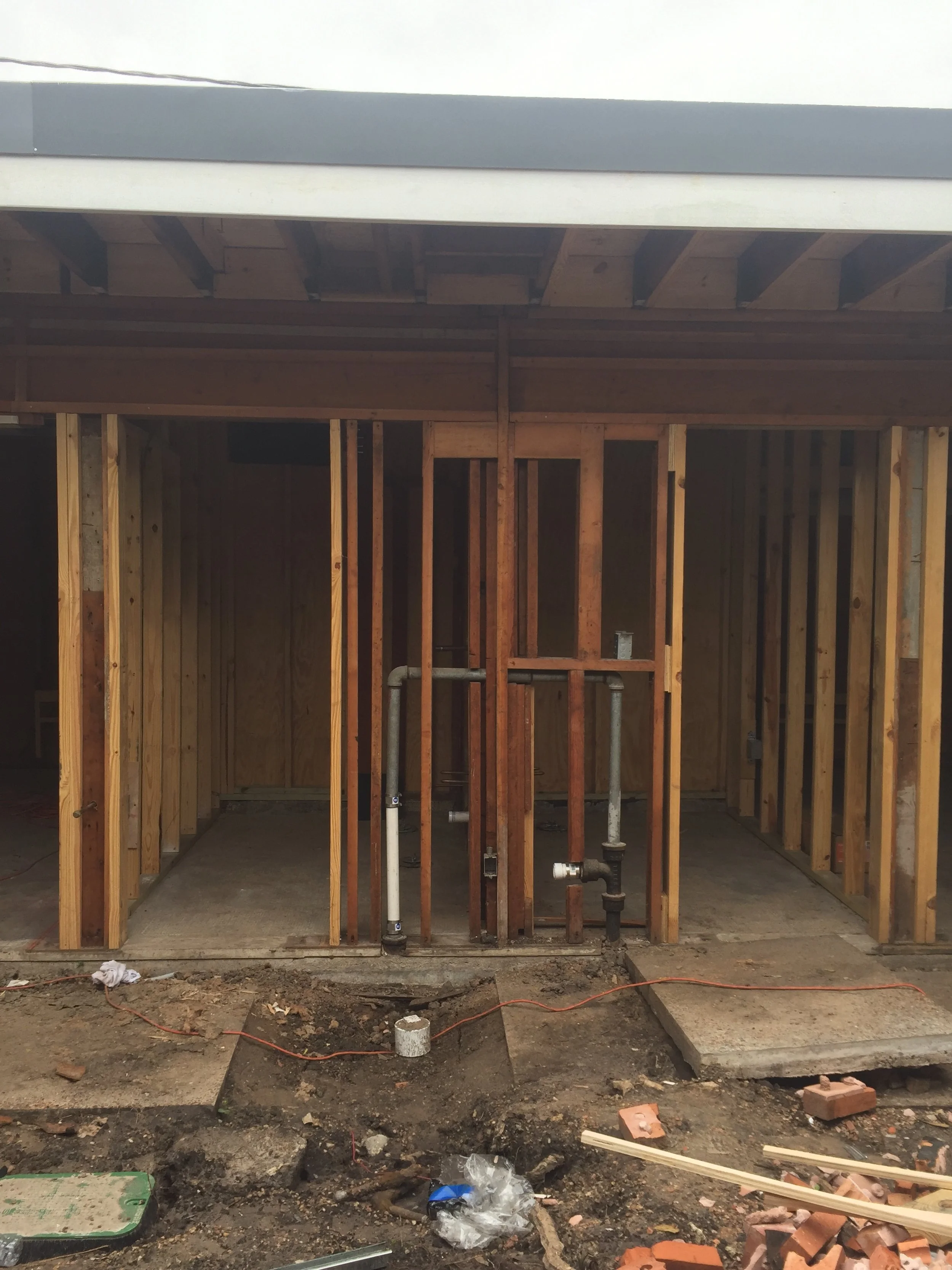 Incomplete construction project with exposed wooden framing, plumbing pipes, and foundation work.