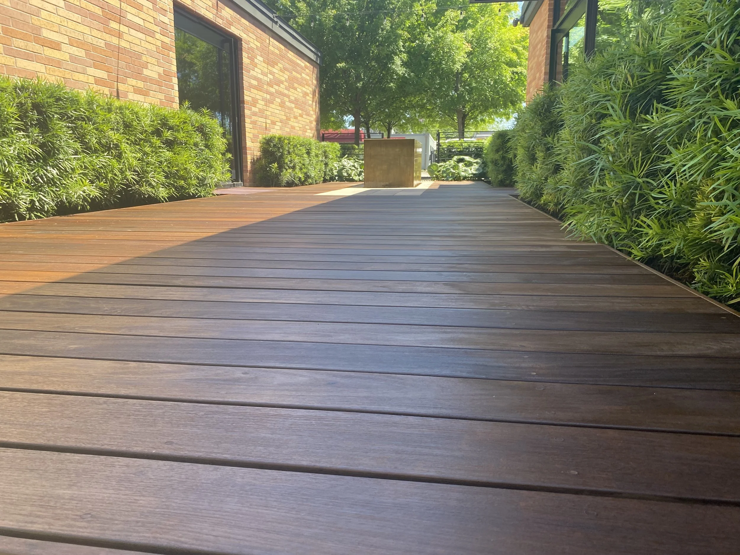 Wooden deck with greenery and brick building in background