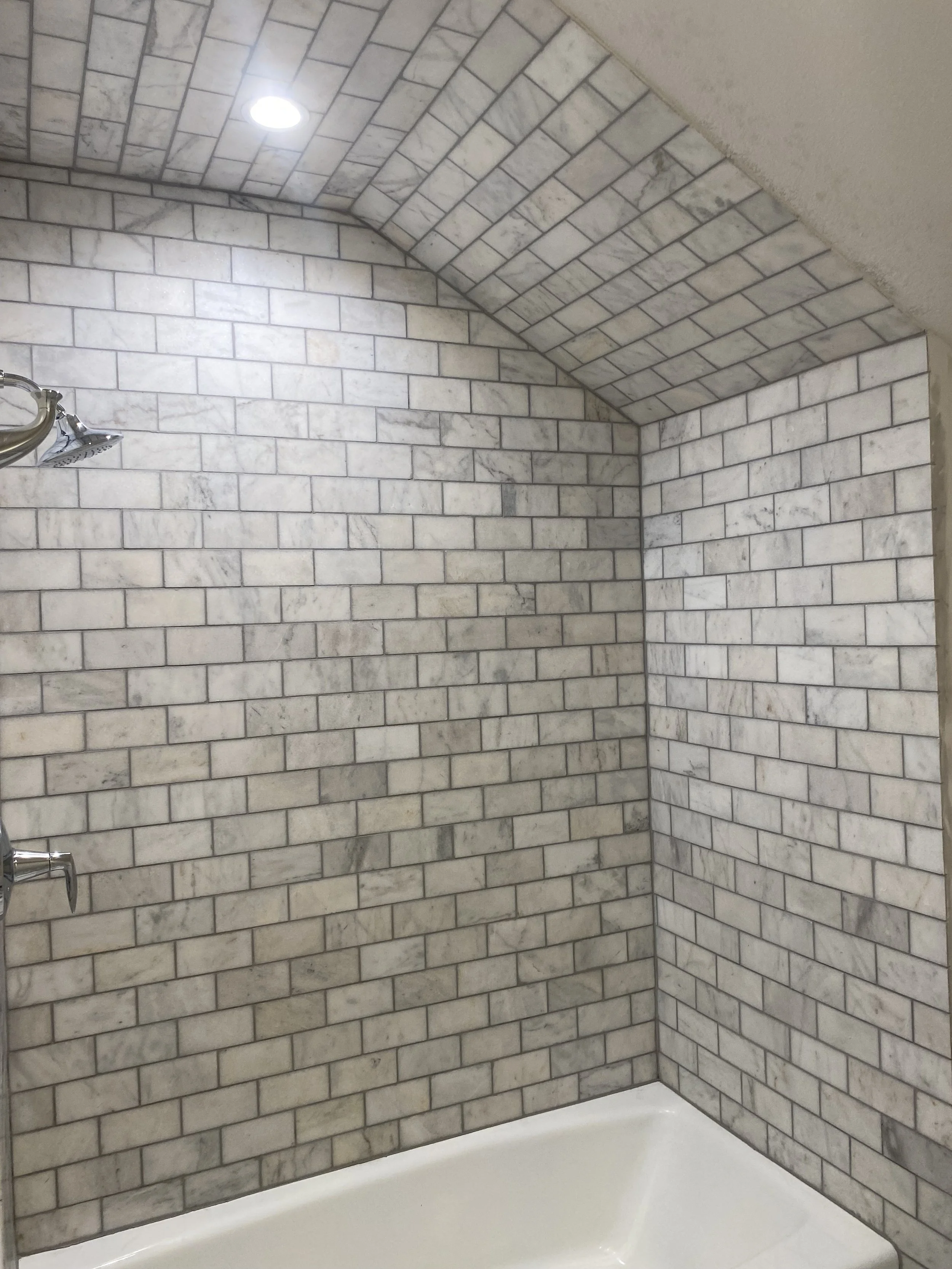Bathroom with marble subway tile walls, arched ceiling, and a white bathtub.