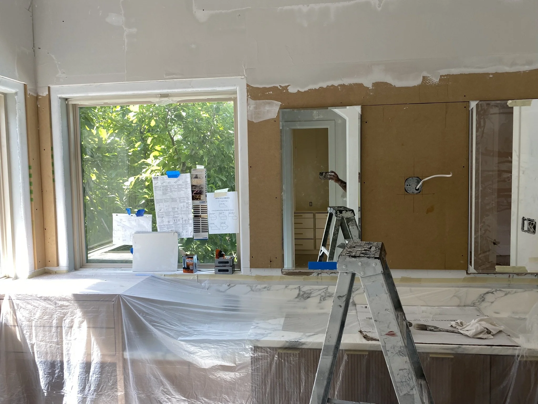 Home renovation scene with ladders, covered windows, and construction materials indoors.