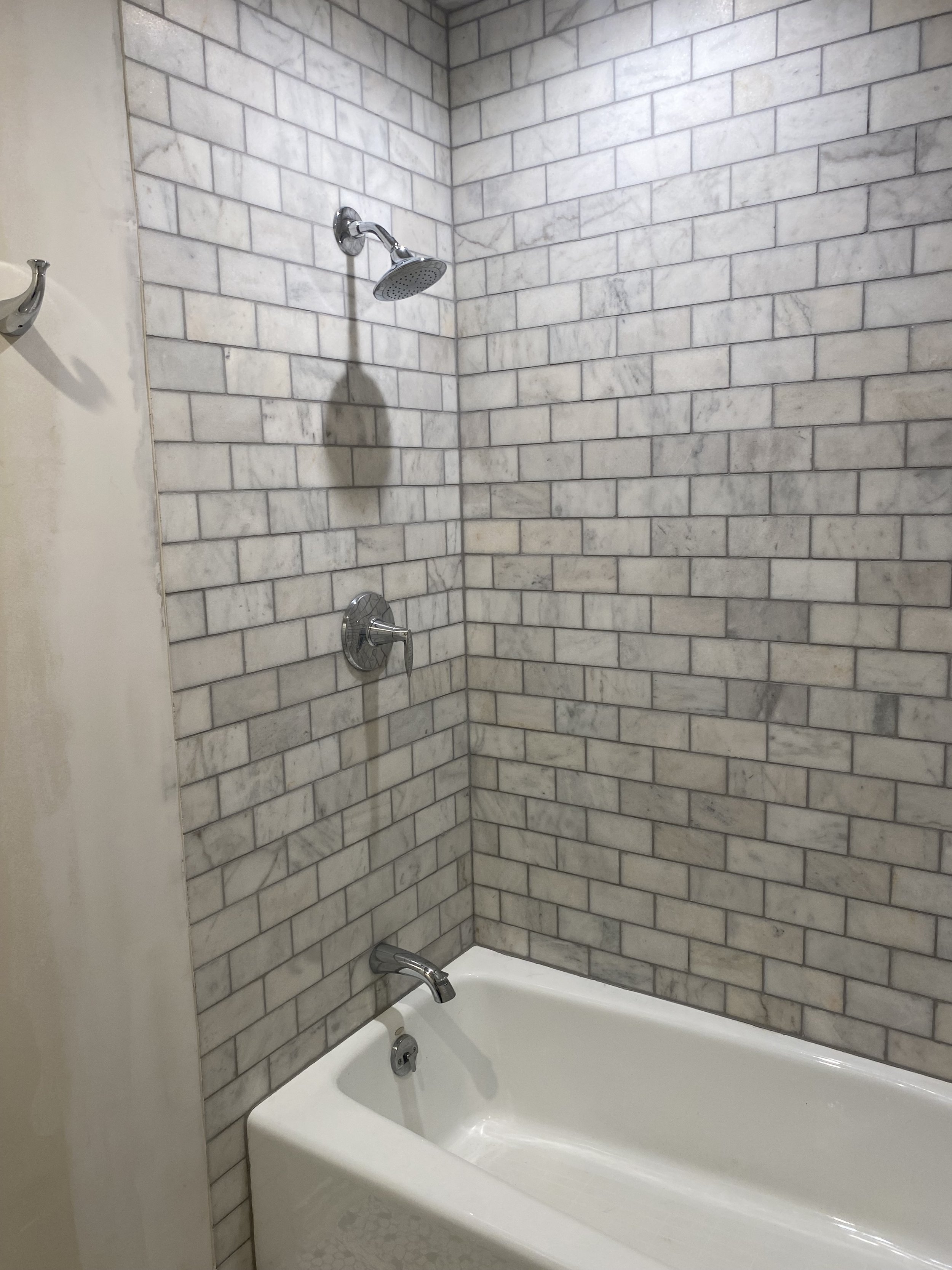 Bathroom with marble-tiled walls, bathtub, and chrome fixtures.