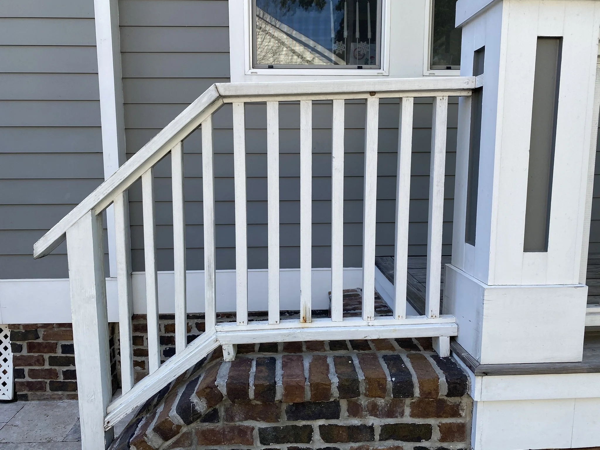 White wooden railing on brick steps in front of a gray house with a window.