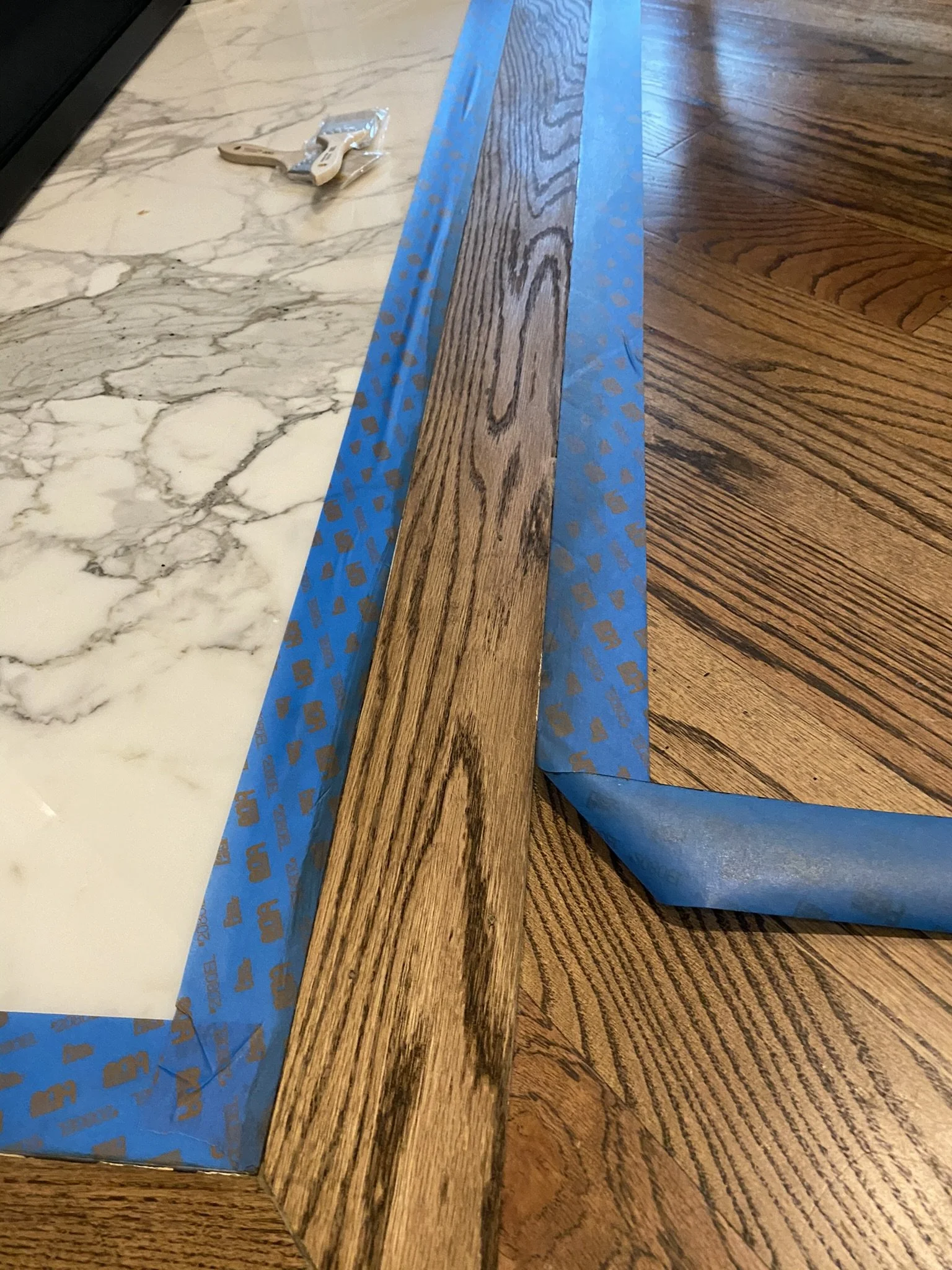 Wood floor with tape border next to white marble tile
