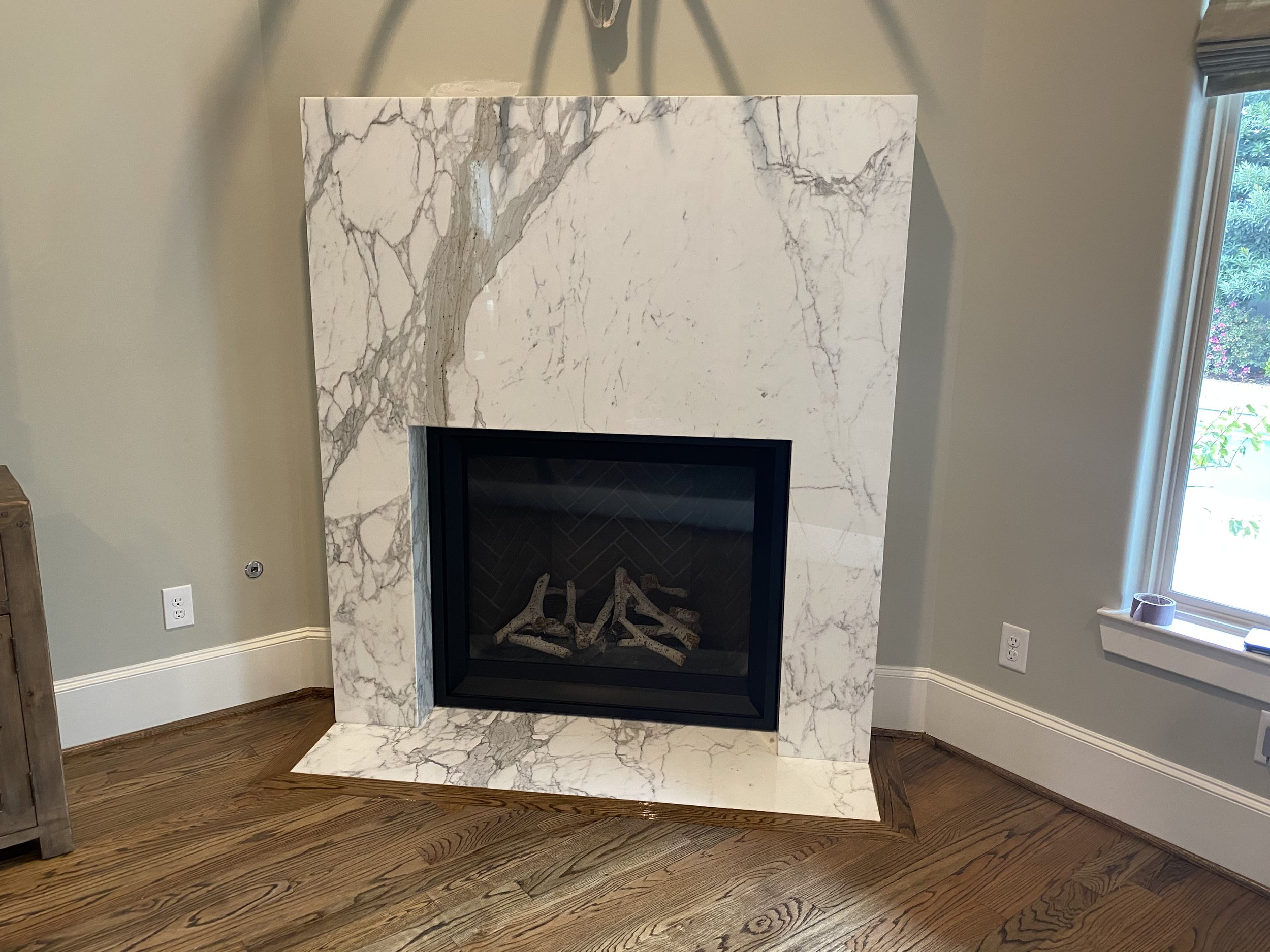Modern marble fireplace with wood flooring in a living room, featuring a large marble surround and a black firebox.