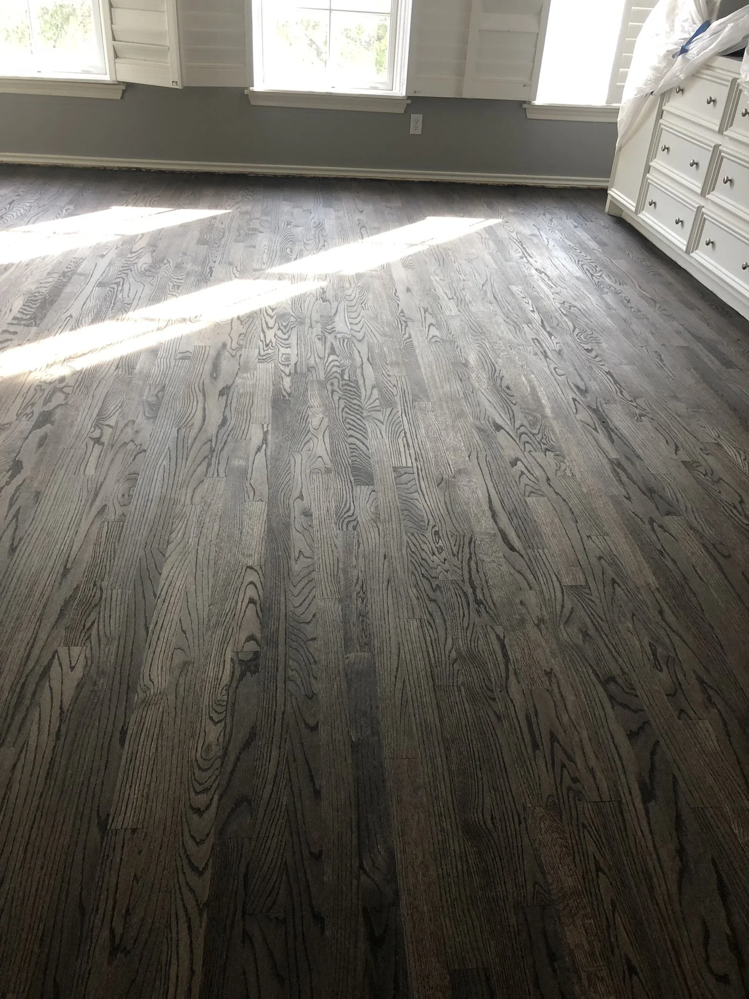 Room with gray hardwood flooring, white walls, and a white dresser partially visible.