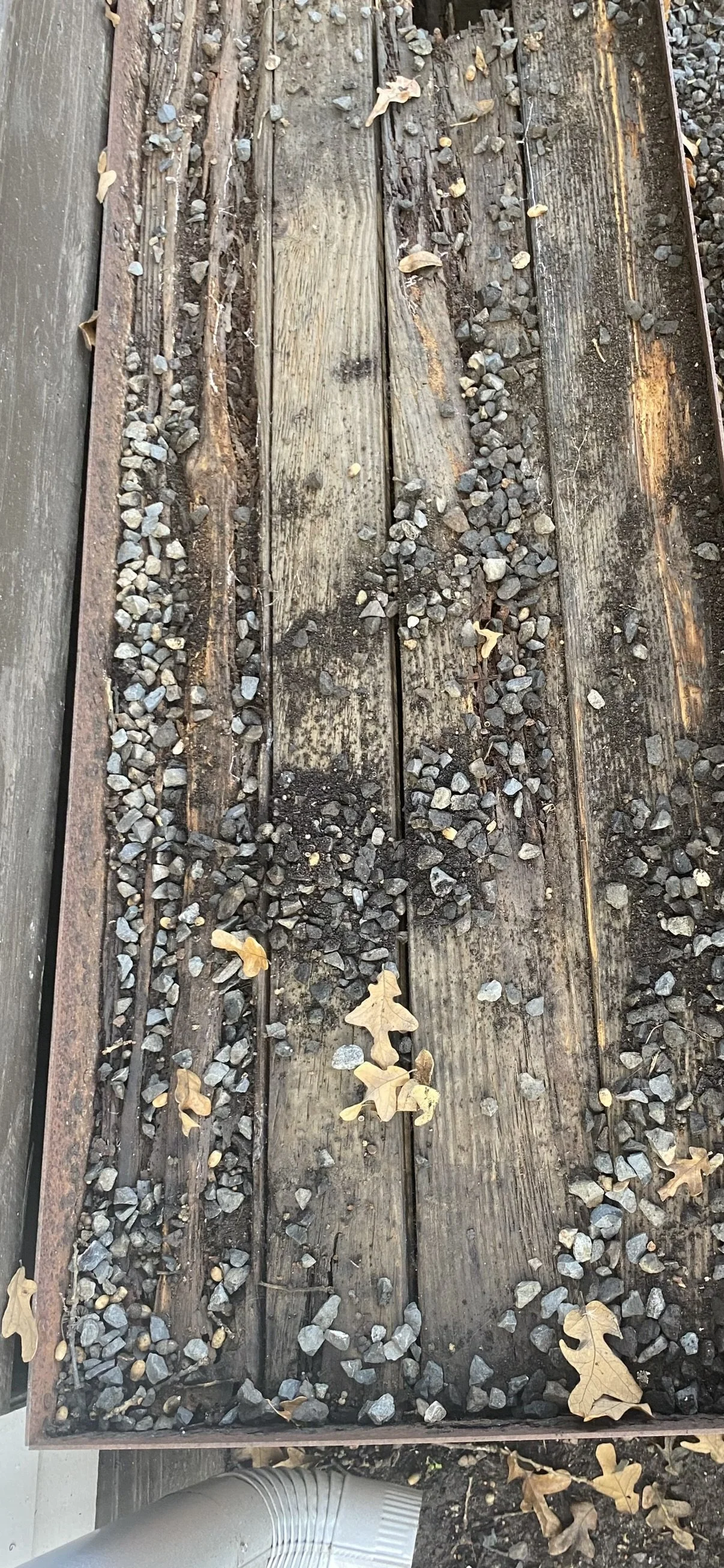 Close-up of weathered wooden railroad ties with scattered gravel and fallen leaves.