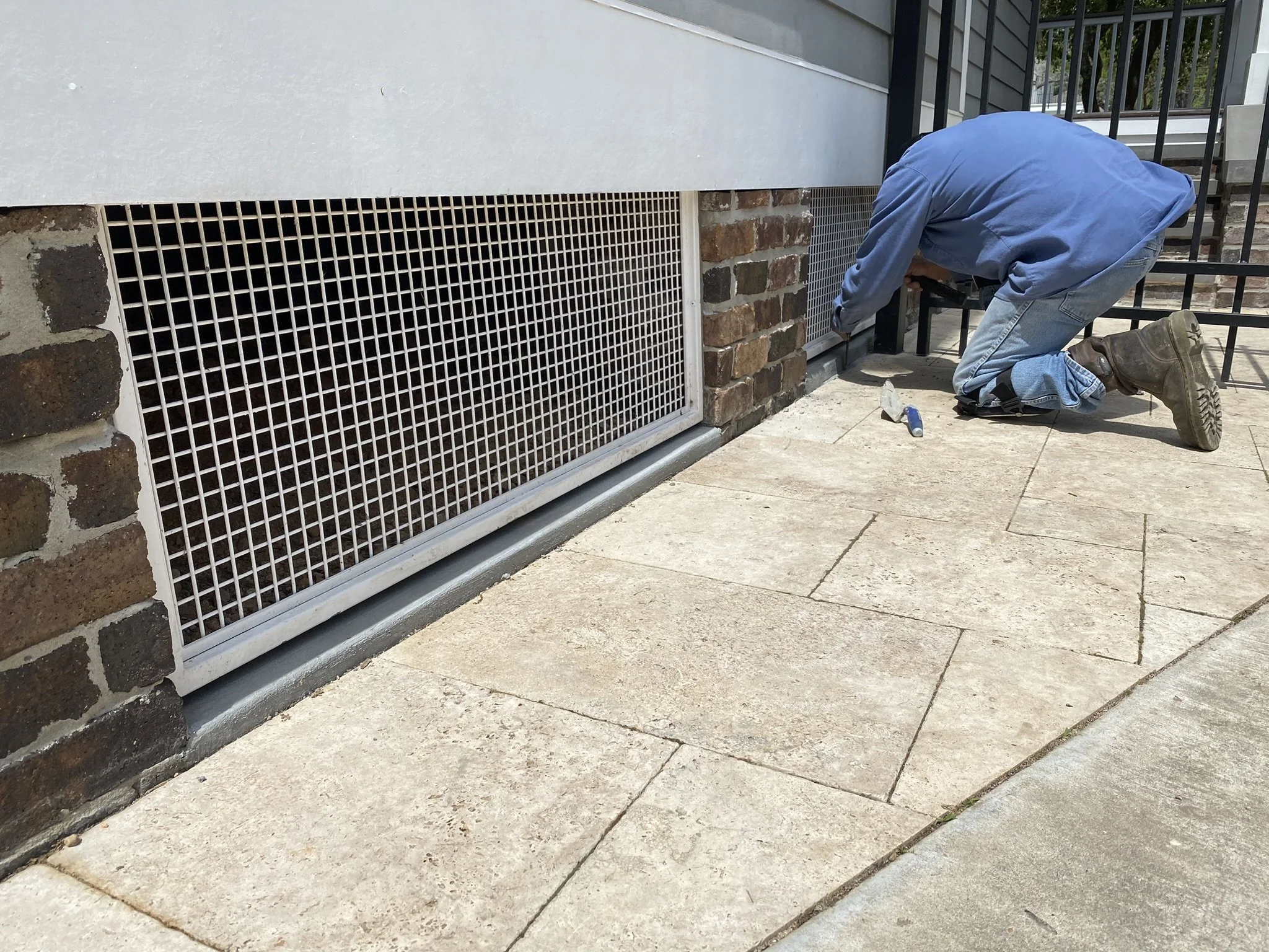 Person in blue shirt and jeans installing a metal fence on a brick and metal building exterior