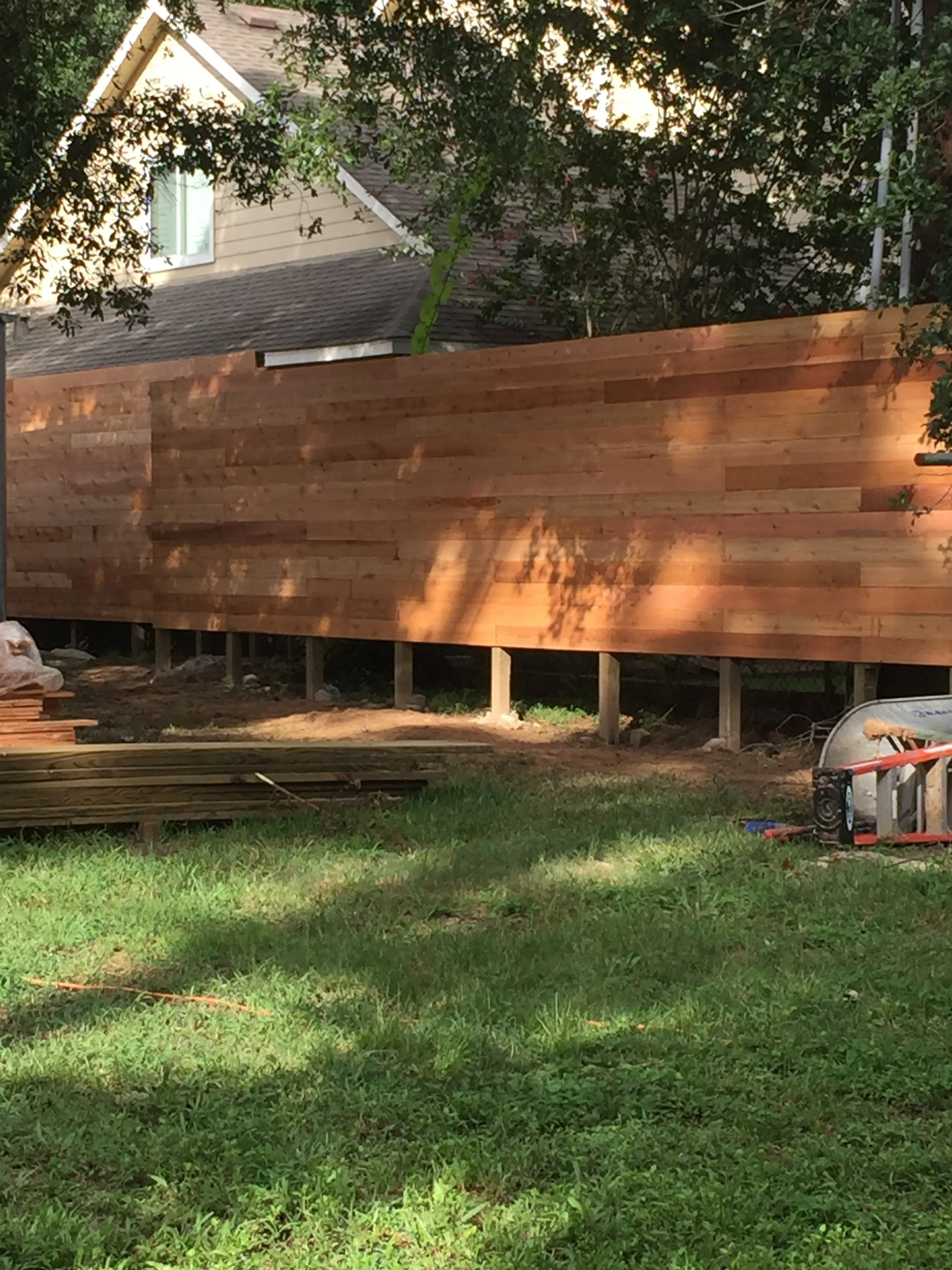 Wooden fence construction in a backyard with a grassy foreground.