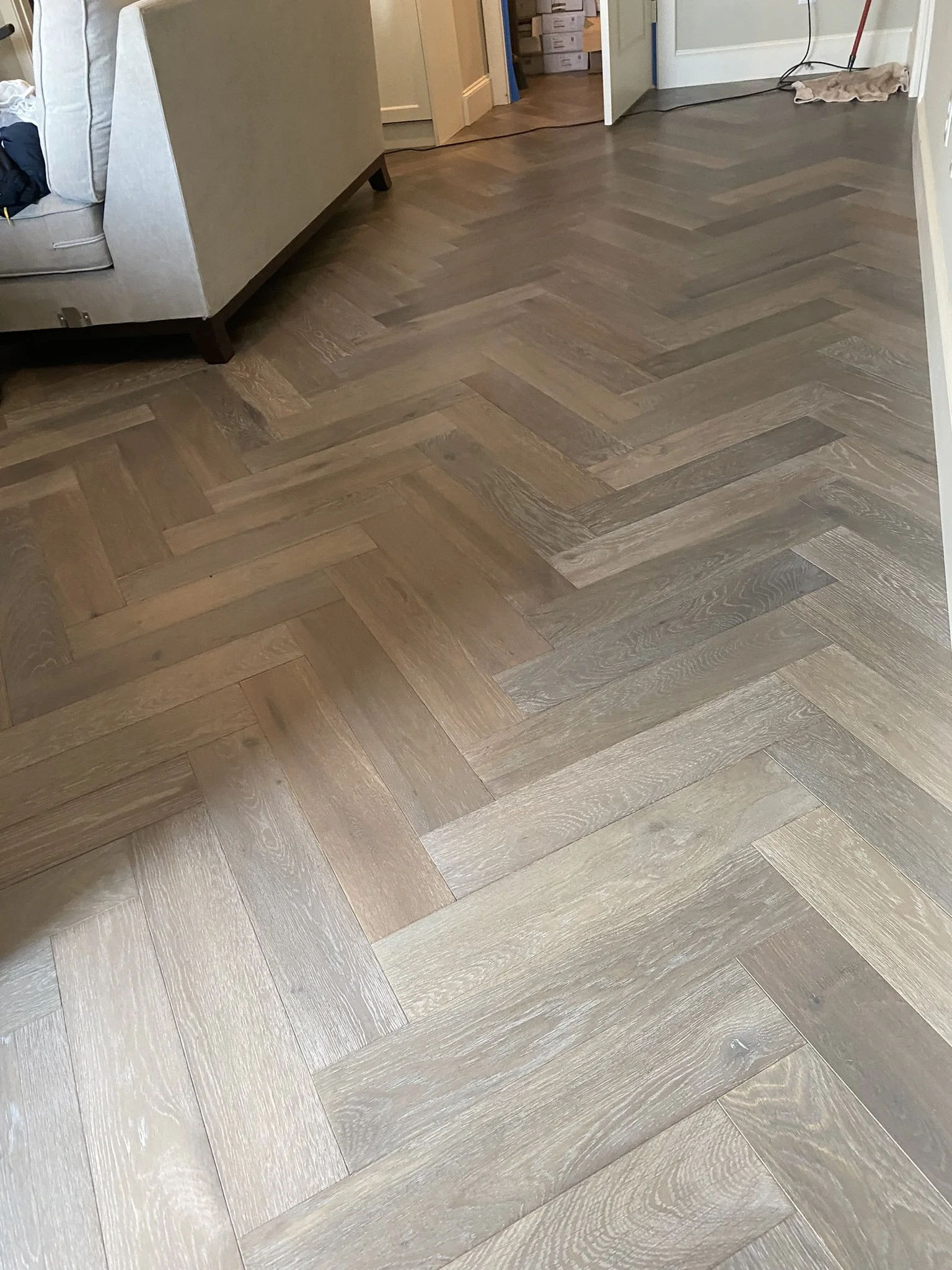 Herringbone wood flooring in a room with a sofa and an open door.