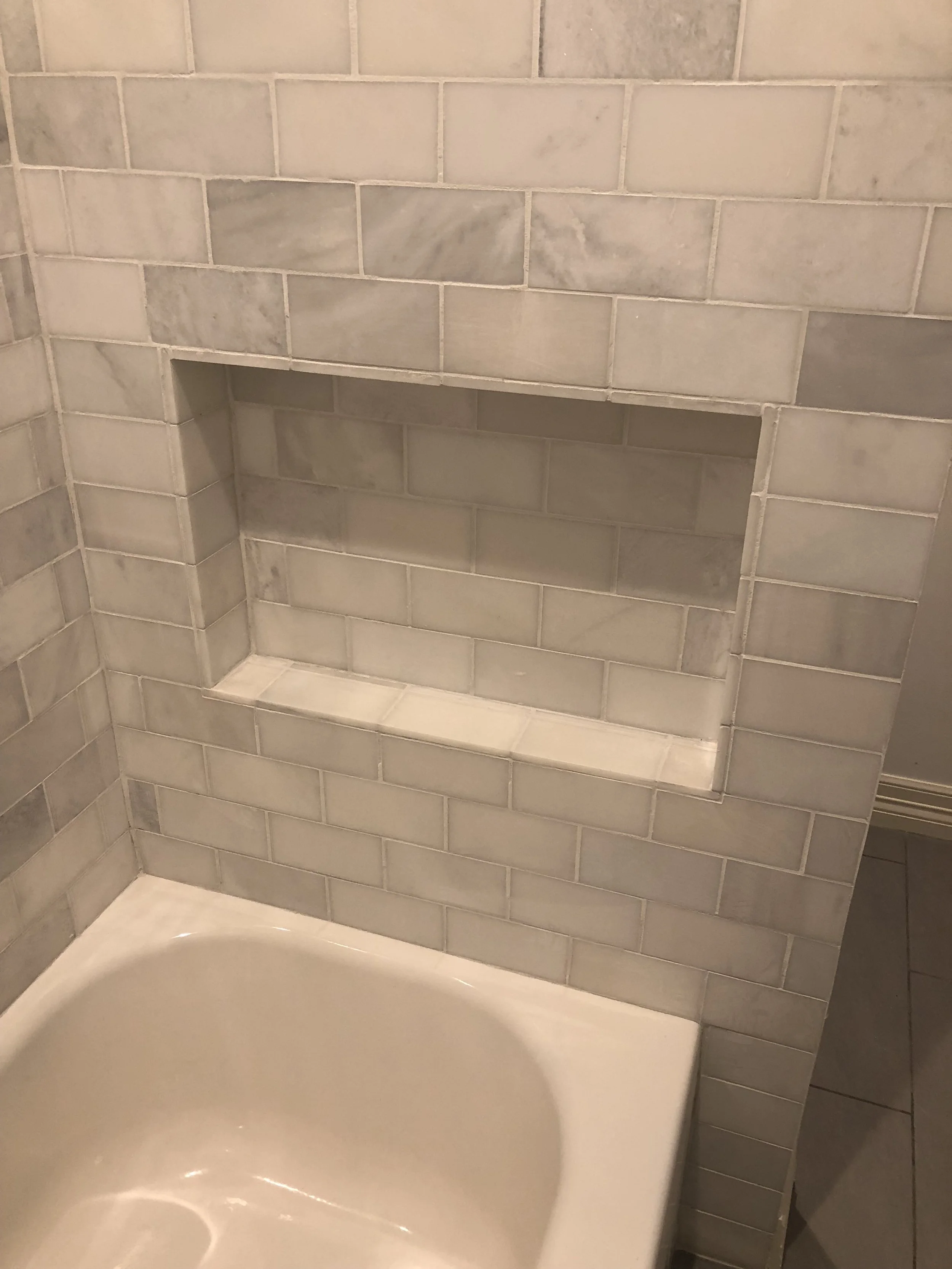 Bathroom with white marble tile wall and bathtub, featuring a built-in shower niche for storage.