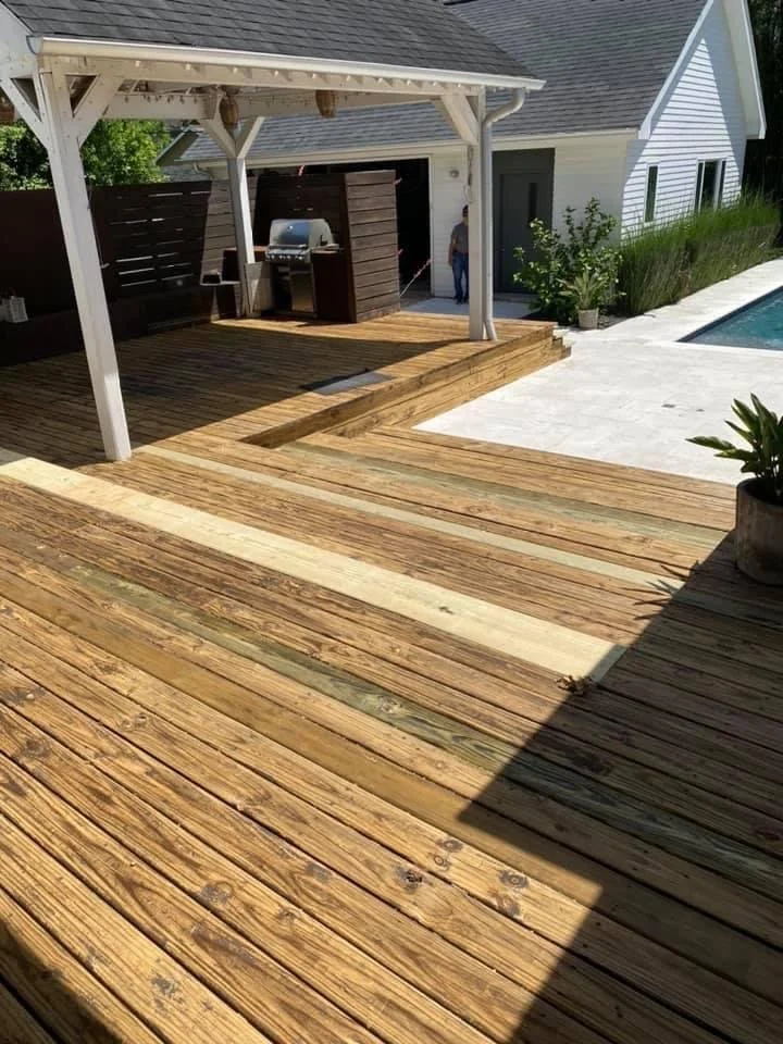 Wooden deck with pergola, grill, and pool in a backyard setting.