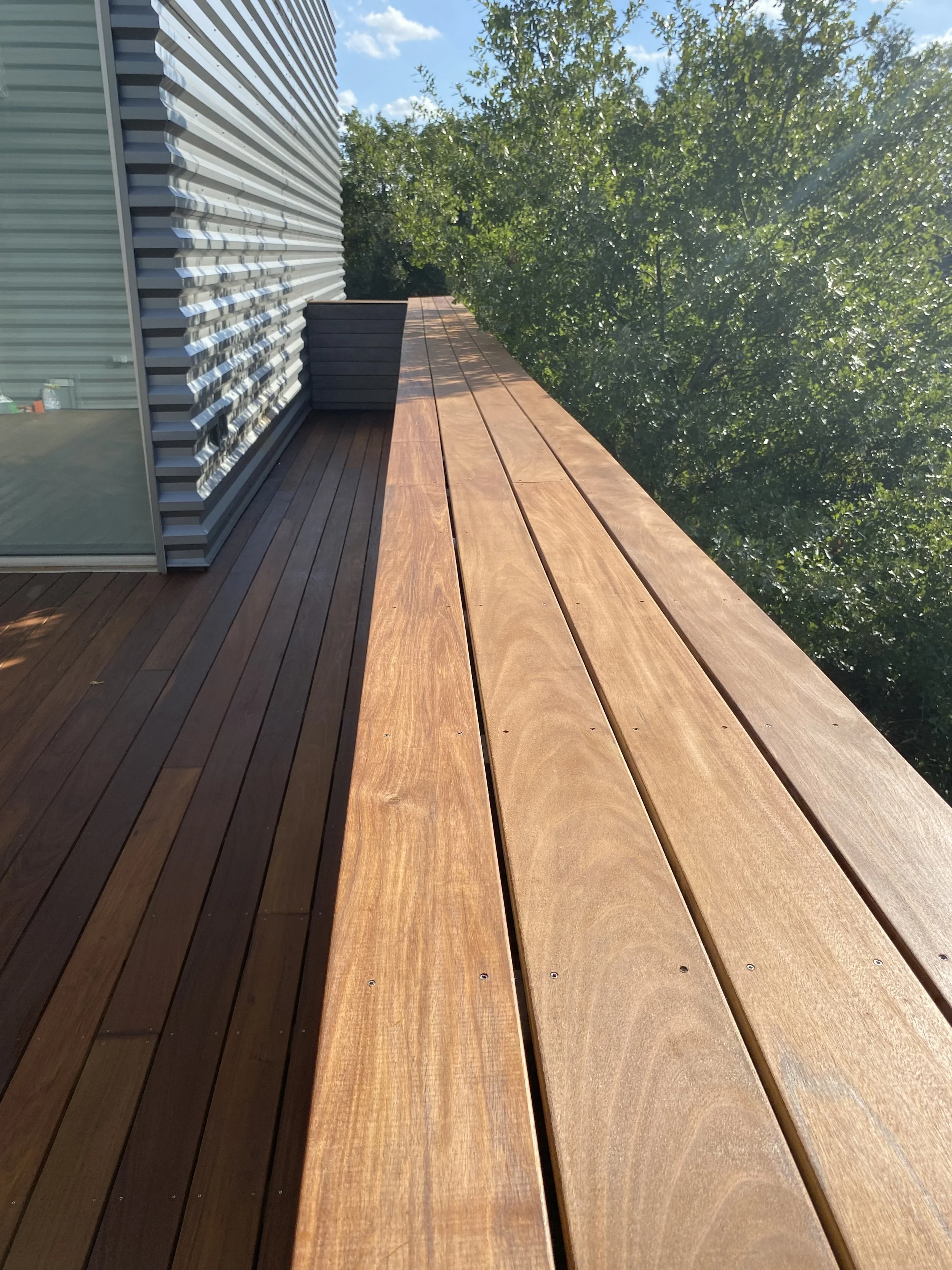 Wooden deck with metal siding and potted plant, surrounded by trees.
