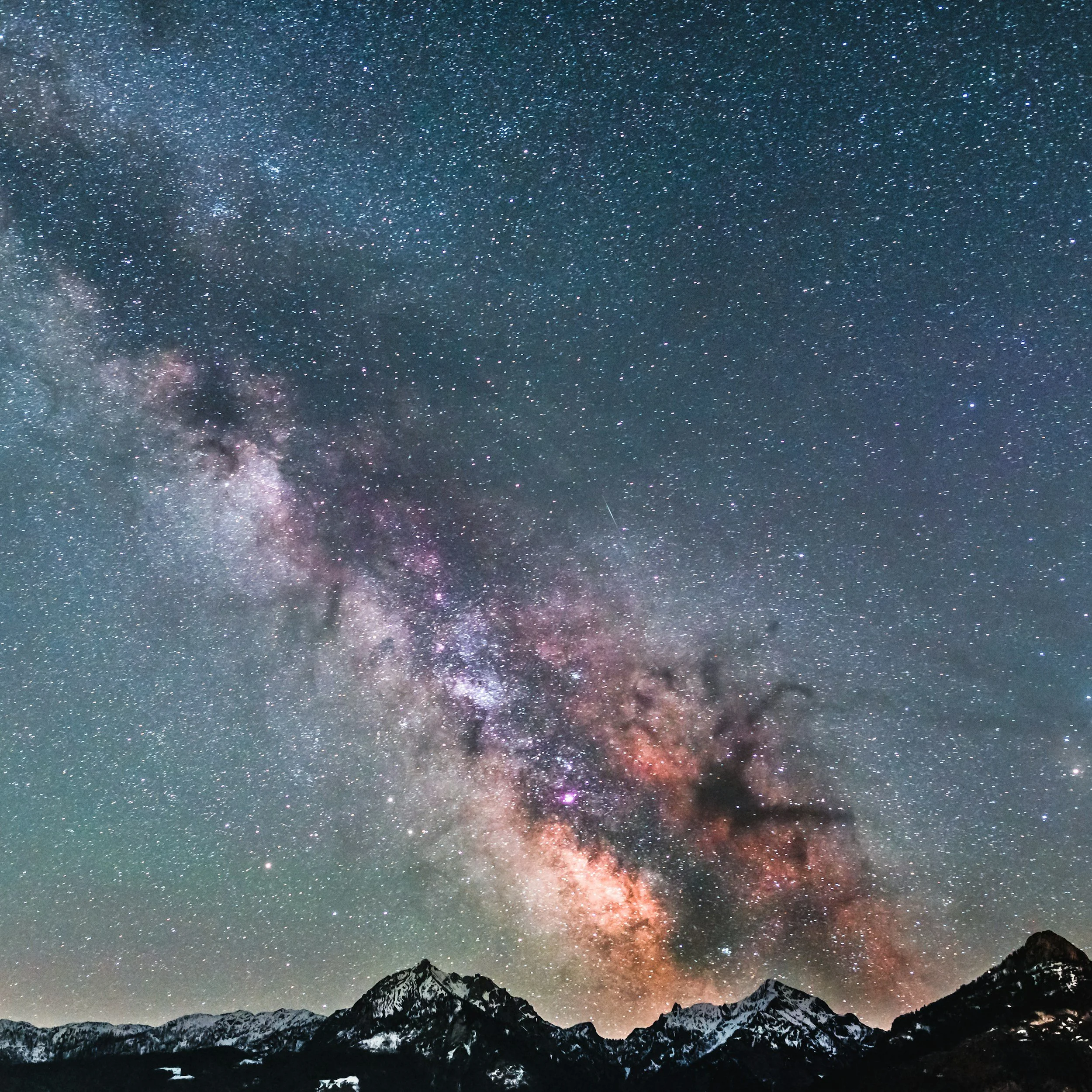 Night sky filled with stars and the Milky Way galaxy above snow-capped mountains.