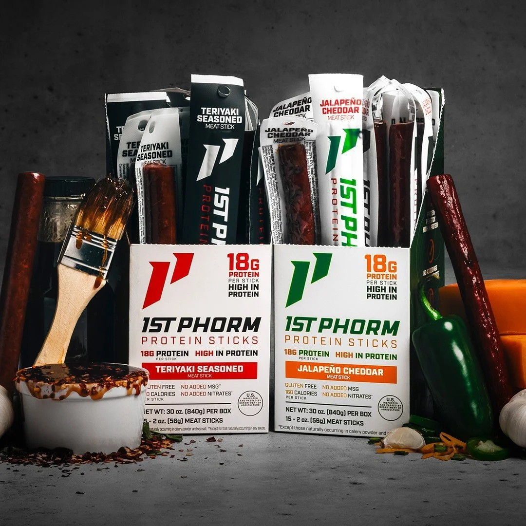 Boxes of 1st Phorm protein sticks in teriyaki seasoned and jalapeño cheddar flavors with meat sticks and spices around them.