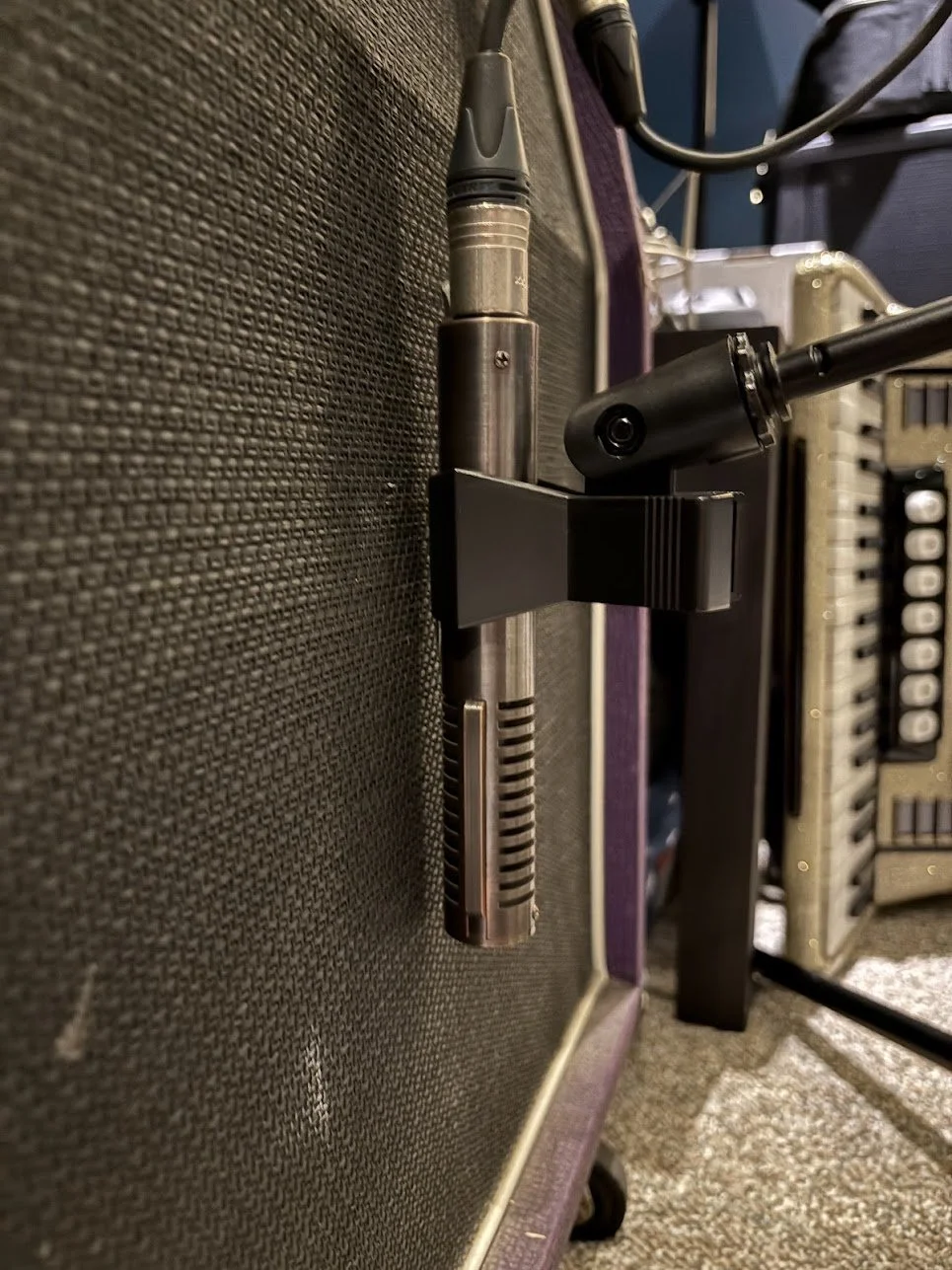 Close-up view of a tube microphone mounted on an amplifier or audio equipment with various cables connected in a music or recording studio.