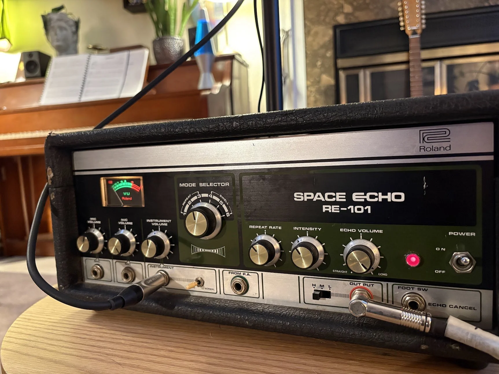 Close-up of a Roland Space Echo RE-101 vintage guitar effects pedal with various knobs, switches, and a VU meter in a music studio.