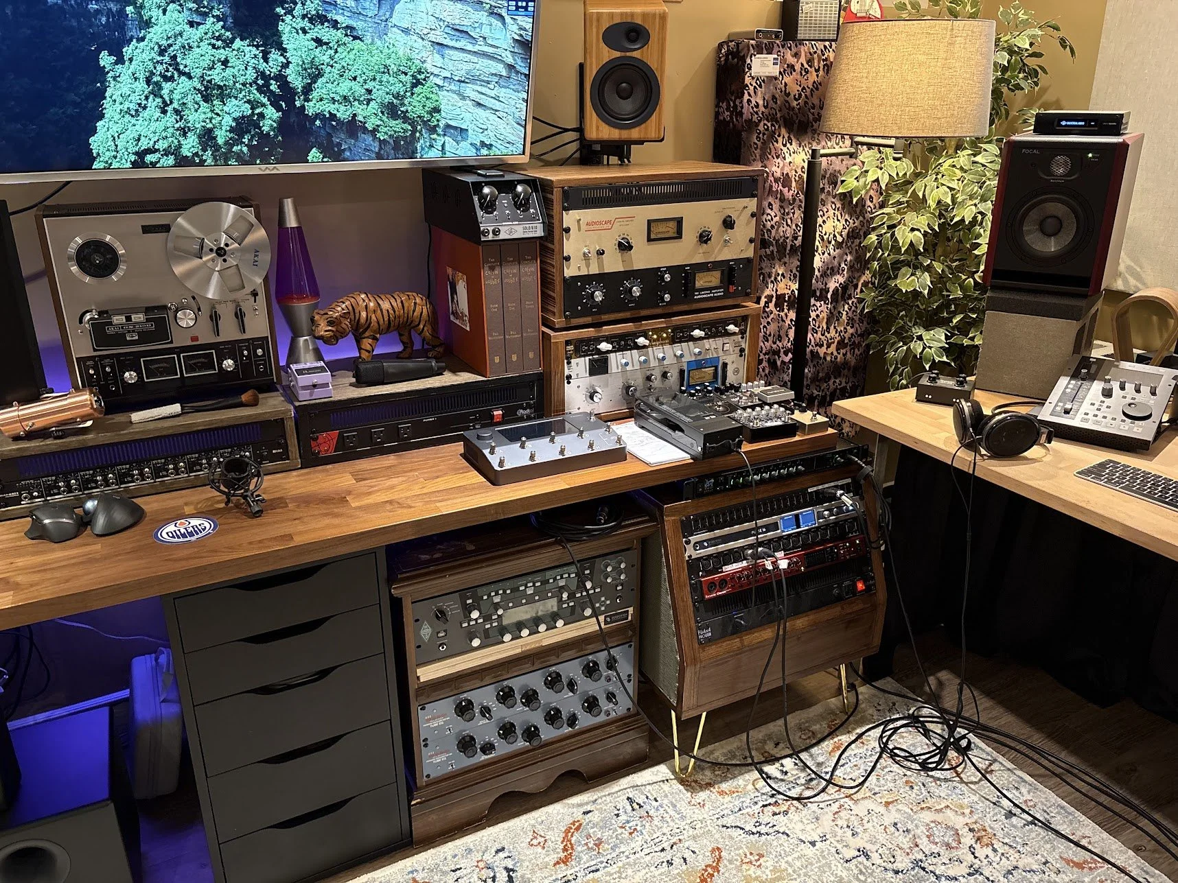 A recording studio with various audio equipment, including a large screen, speakers, mixing consoles, and a lamp surrounded by plants and decorative items.