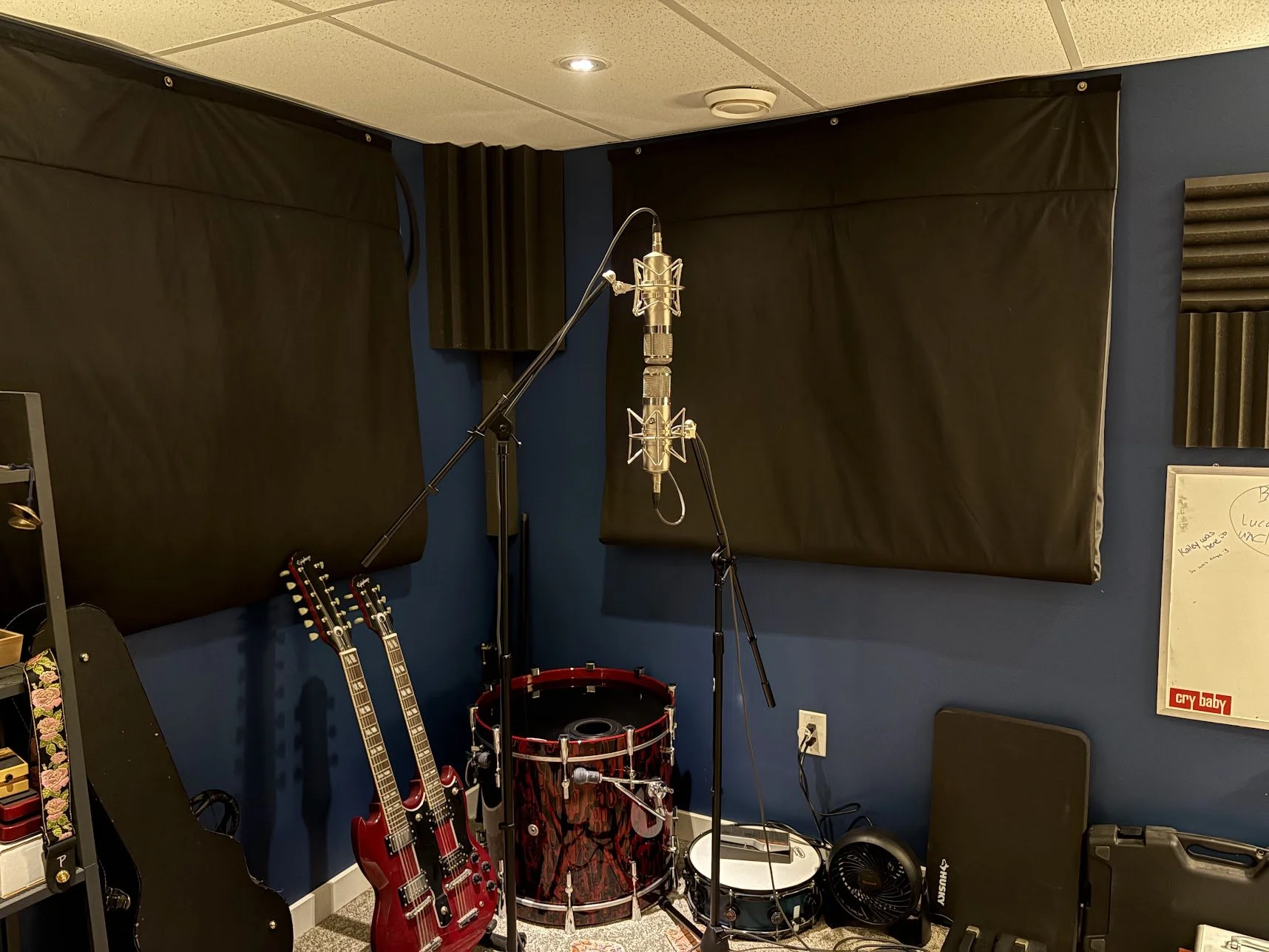 Music studio with guitars, drums, microphones, soundproofing panels, and electronic equipment.