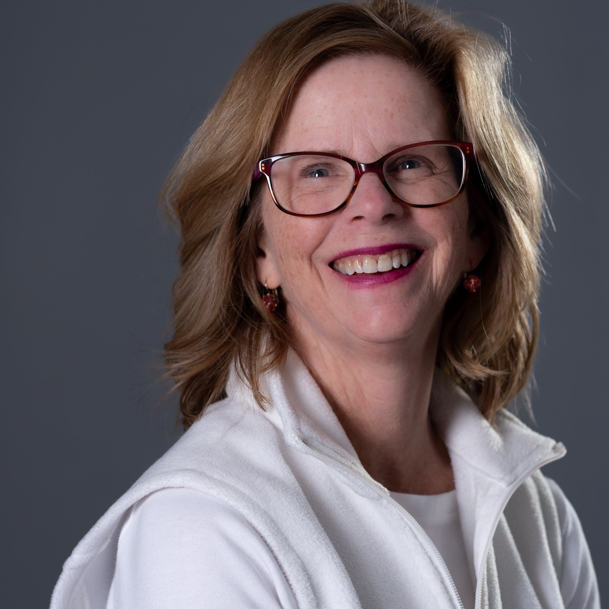 A smiling woman with blonde hair and sunglasses standing outdoors against a rocky background.