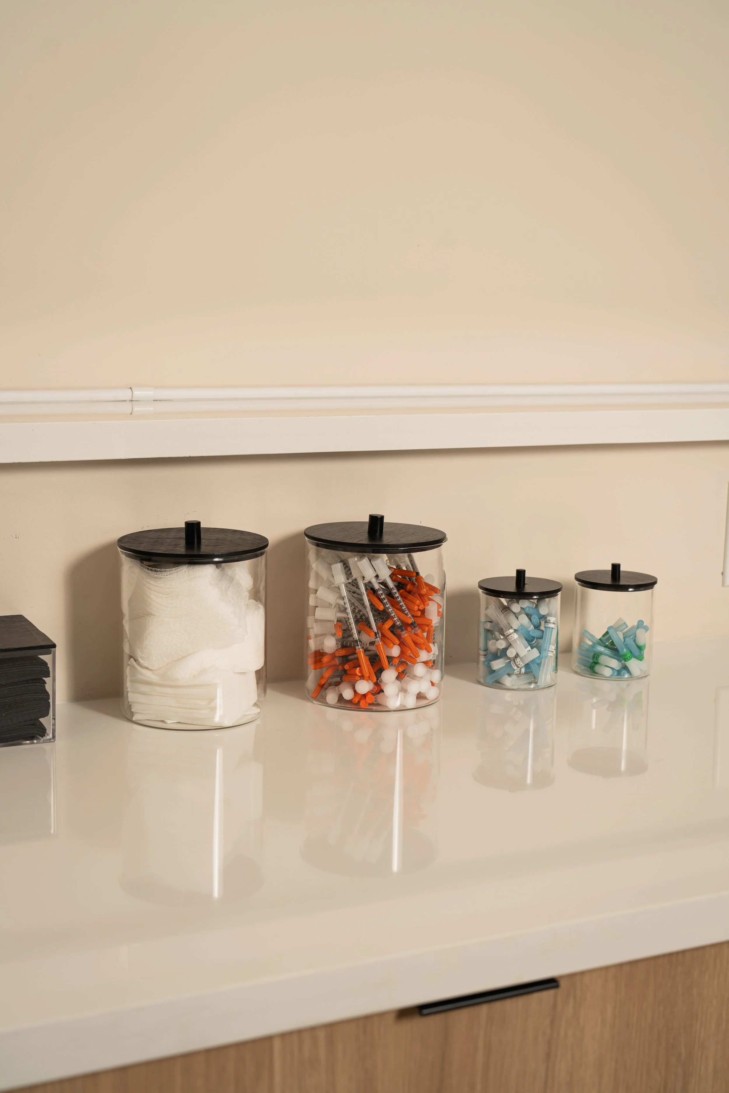 Glass apothecary jars holding gauze, syringes, and needle tips on a treatment room counter.