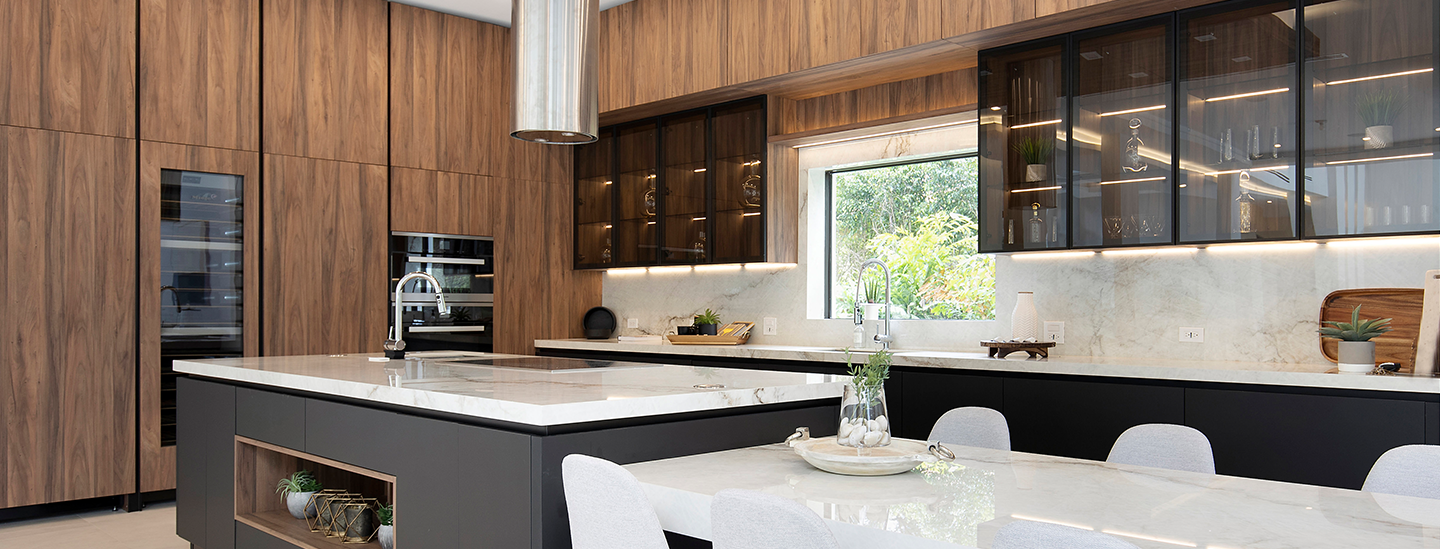 Modern kitchen with wooden cabinets, a white marble island, black cabinetry, and a large window with lush greenery outside.
