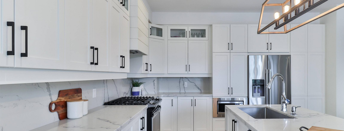 Modern kitchen with white cabinets, marble countertop, stainless steel appliances, and a black and gold light fixture.