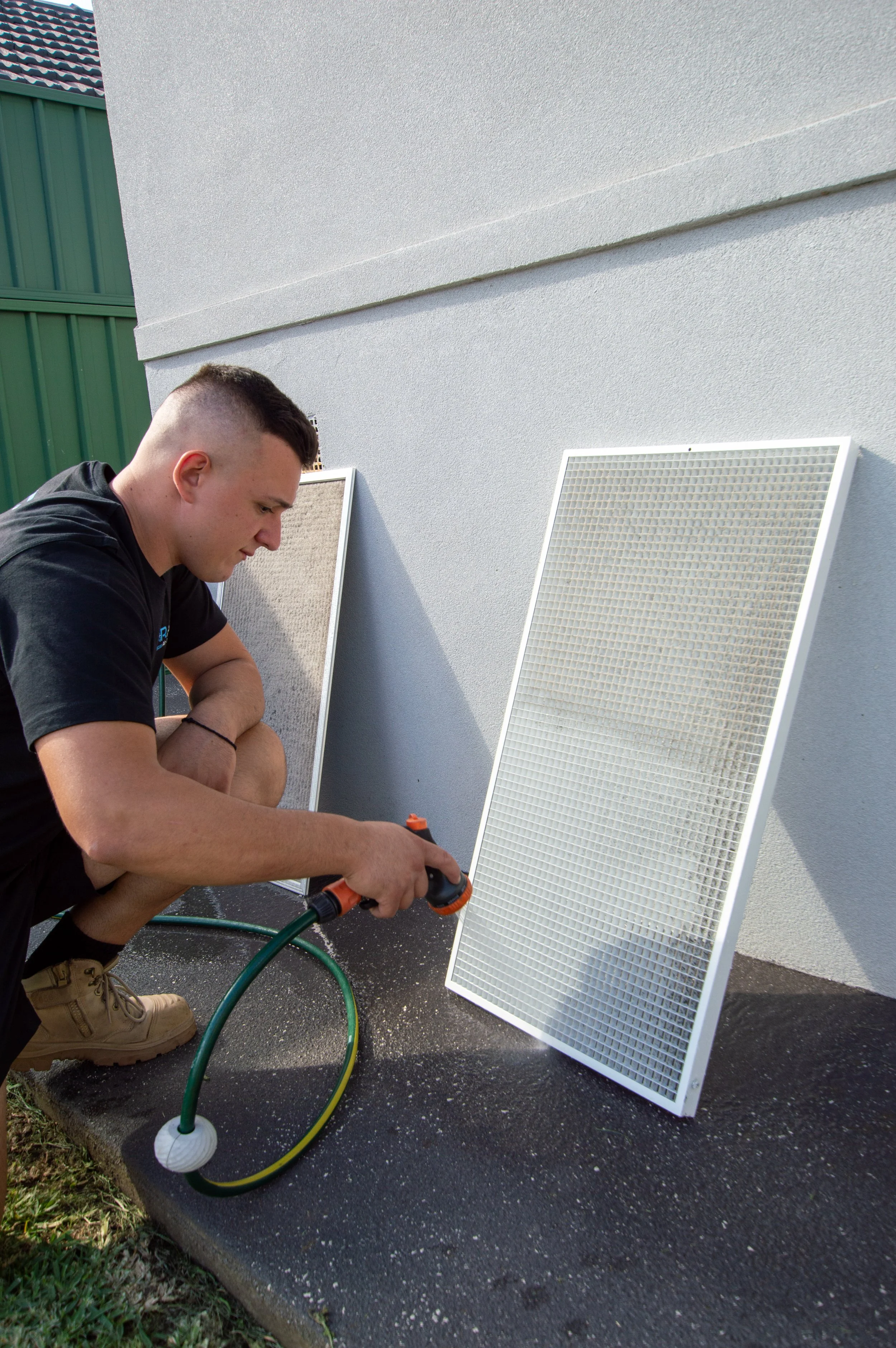 Man cleaning air conditioner filters with a hose outdoors