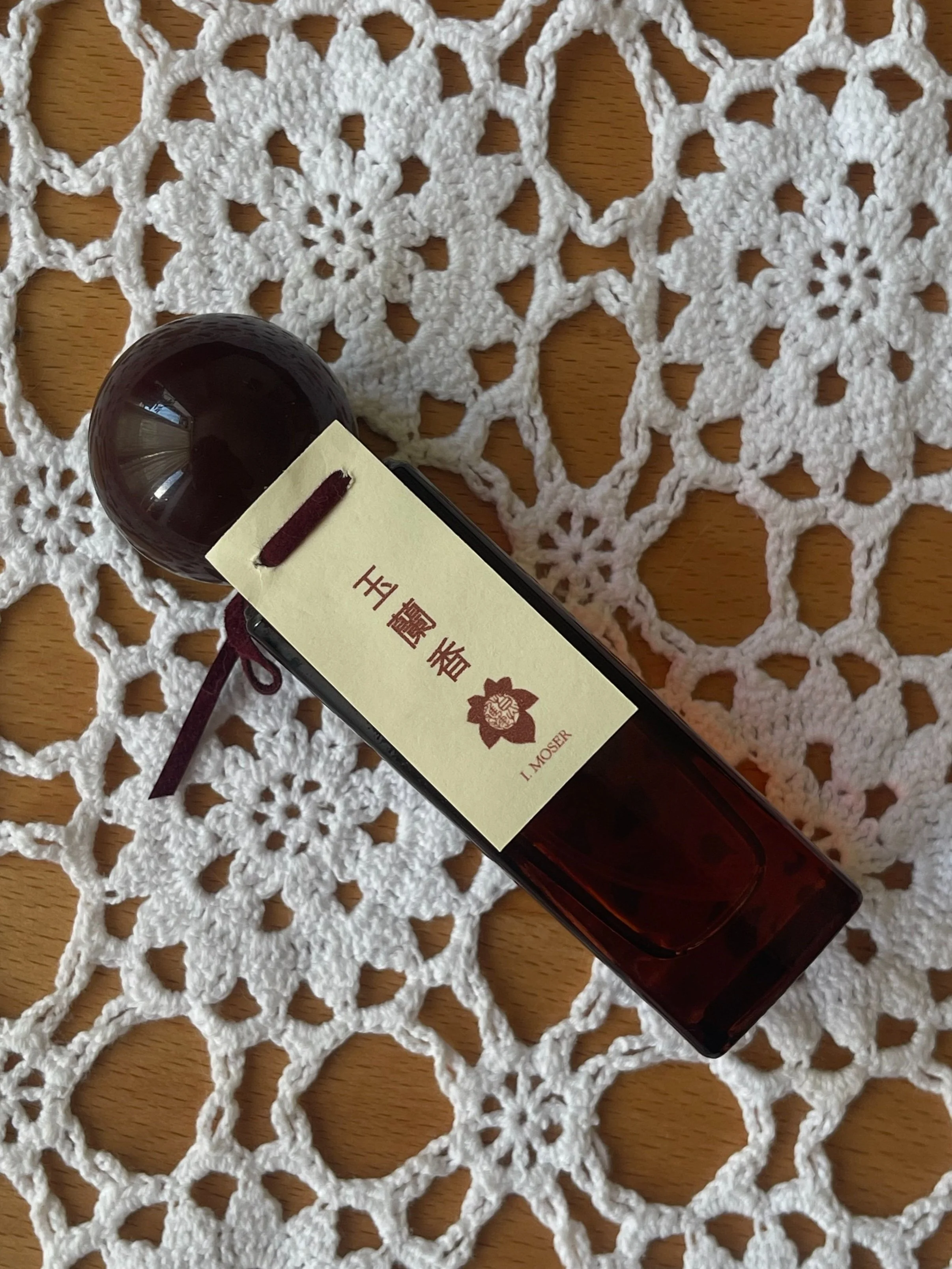 A brown glass bottle with an ornate label featuring gold Chinese characters and floral design, set on a white crochet lace background.