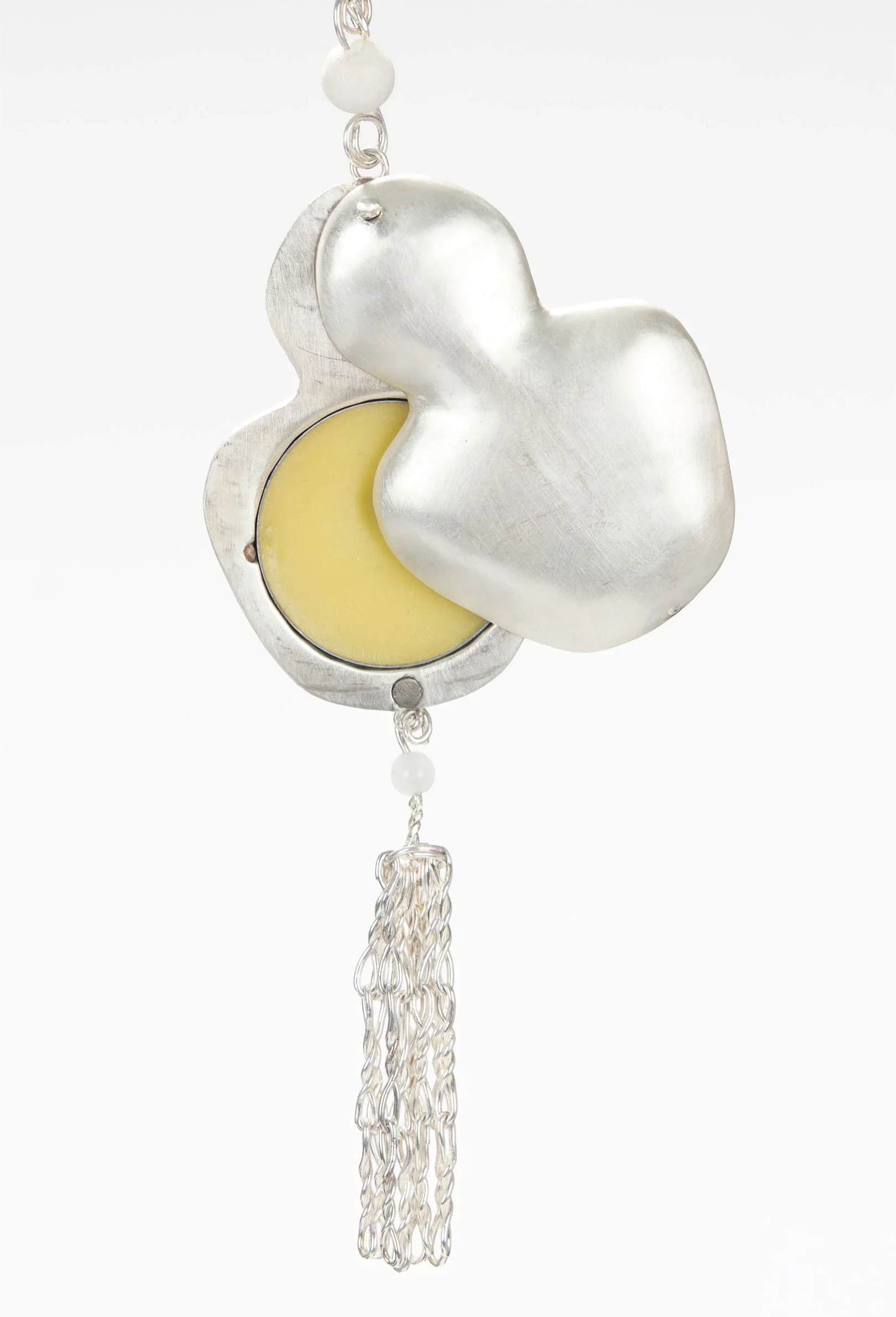 A silver keychain with a moon-shaped yellow centerpiece, covered by a silver heart-shaped charm, with a dangling silver chain and bead.