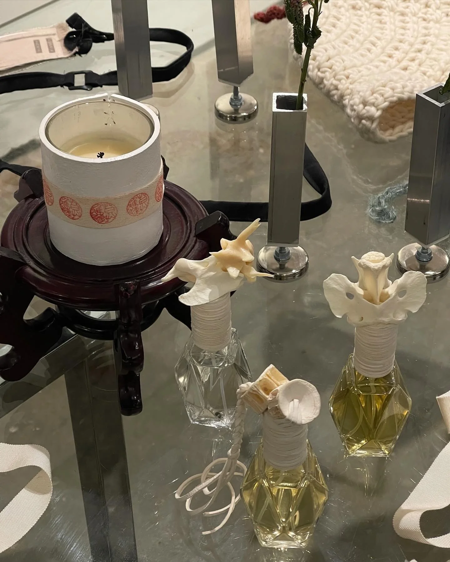 Decorative candle on a wooden stand with three ornate perfume bottles nearby on a glass table.