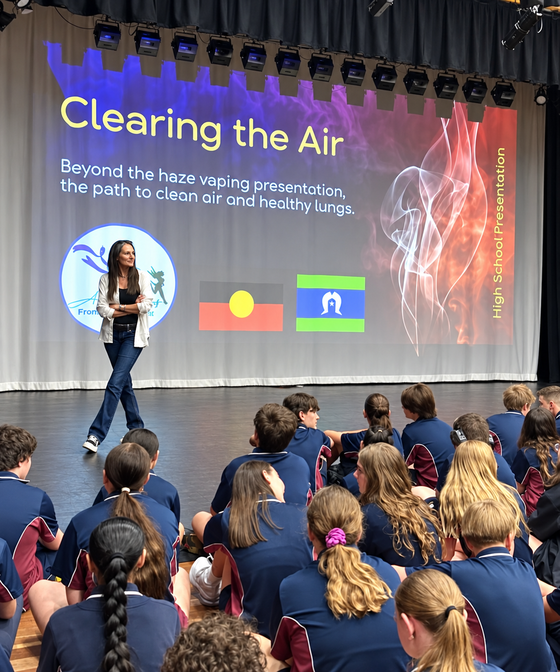 Azelene Williams presents a talk titled 'Clearing the Air' on stage to an audience of students in school uniforms. The slide behind her shows a smoky graphic, flags, and text about the path to cleaner air and healthy lungs.