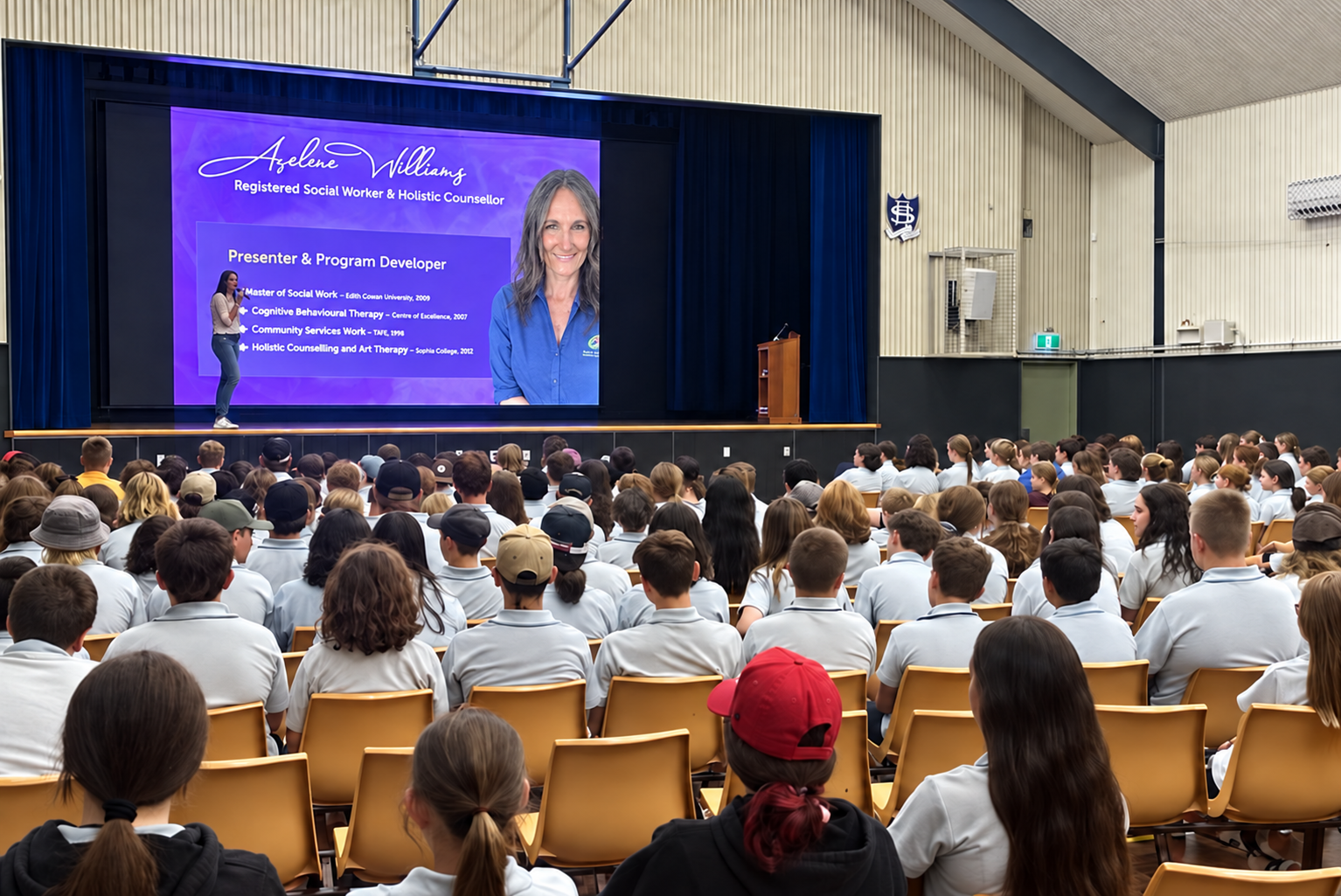Azelene Williams is giving a presentation on stage in front of a large audience of students in a school auditorium. The projection screen displays her name, roles, and credentials.