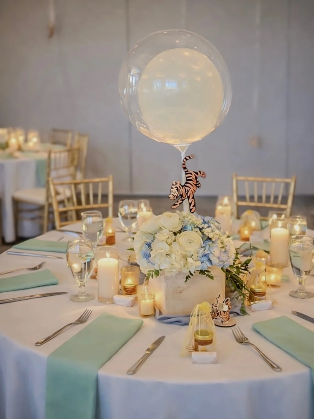 Decorated banquet table with a floral centerpiece, a large clear balloon with a tiger inside, surrounded by candles and place settings for a celebration or event.