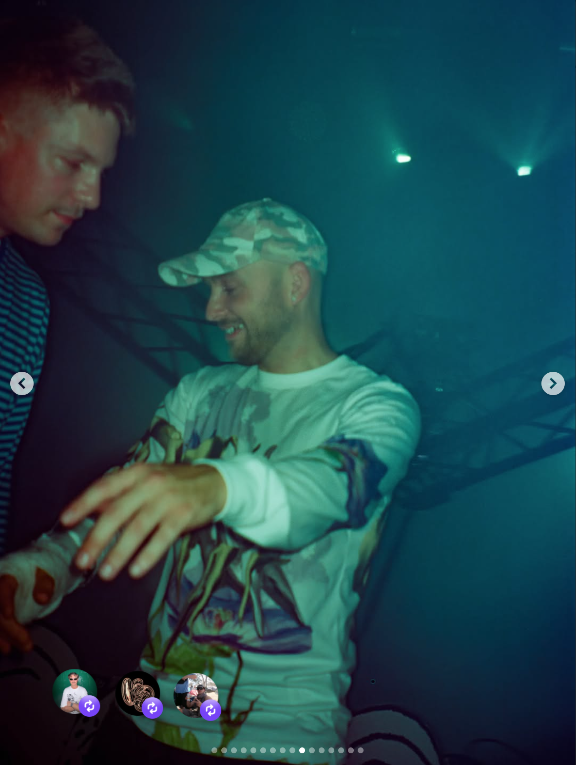 Two men sharing a moment, one wearing a camo hat and the other in a striped shirt, in a dark, foggy setting with green lights.