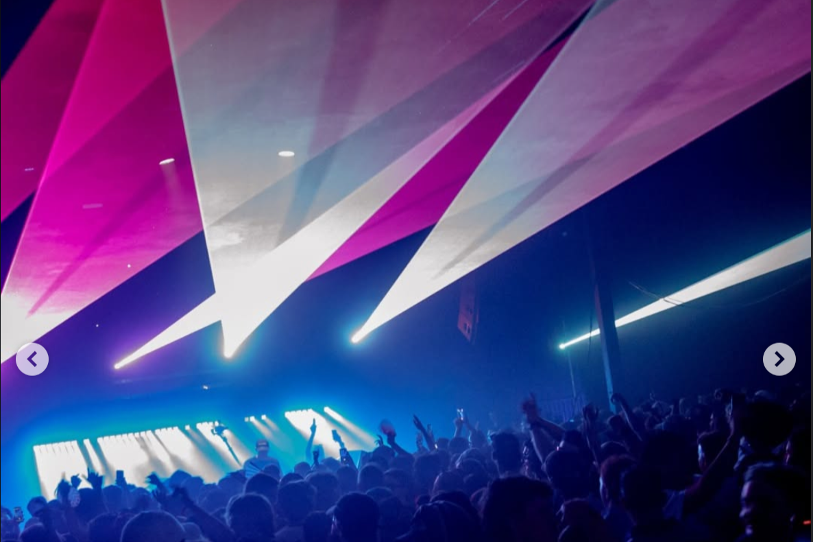 Crowd at a concert or club with colorful light beams and blue lighting.