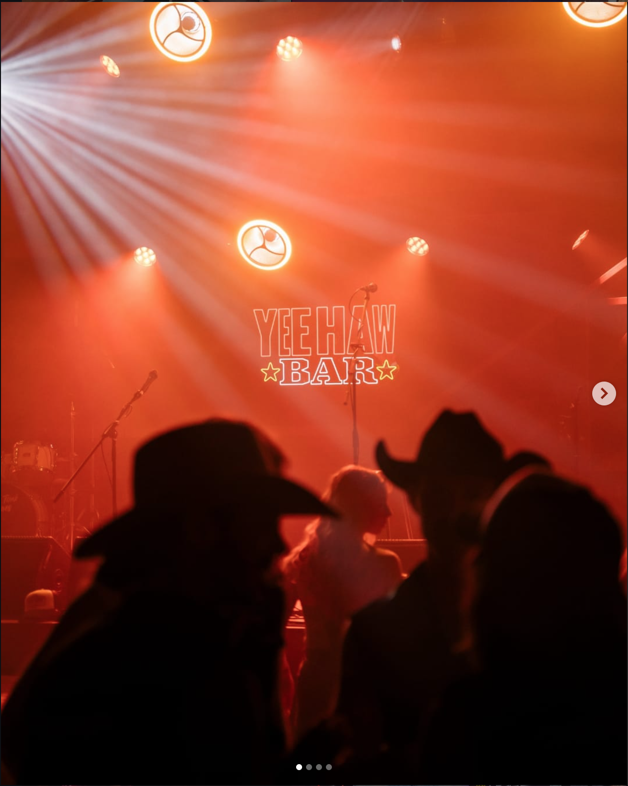 A stage with red lighting, featuring a sign that reads 'Yee Haw Bar,' microphones, and musical instruments, with silhouettes of people in the foreground.